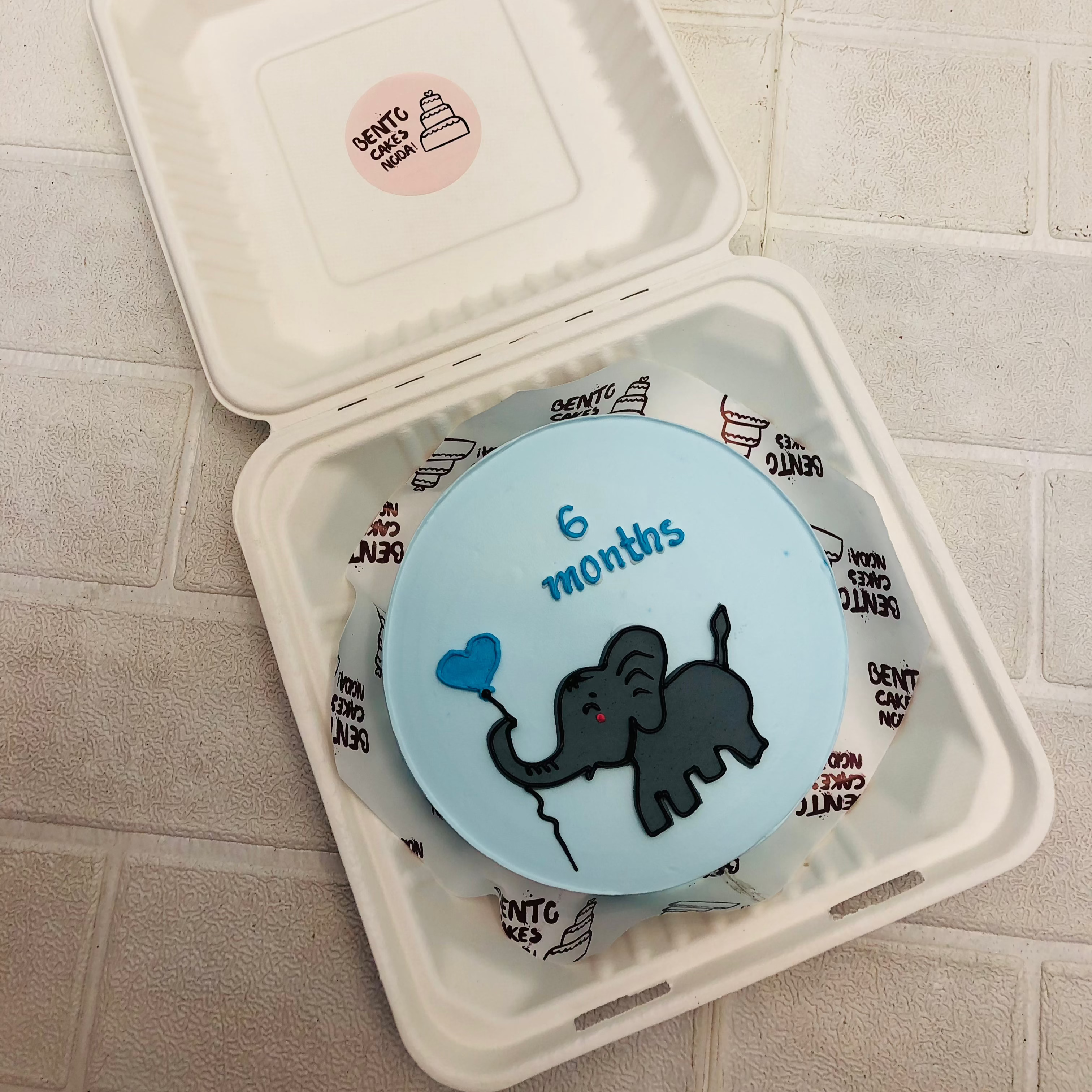 A light blue cake with a cute grey baby elephant taken balloon.