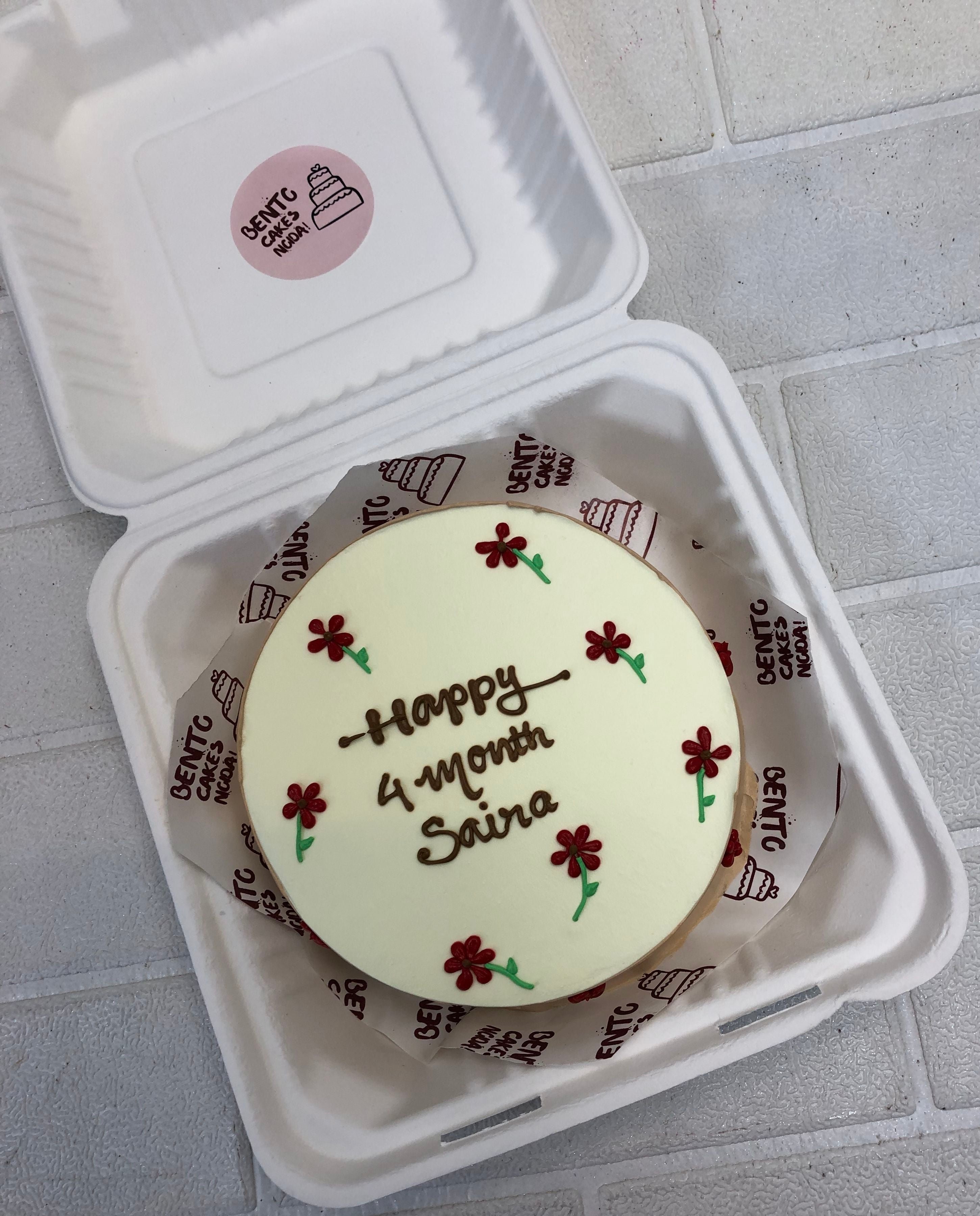 A red floral design on white cake for '4 Months Saira'.