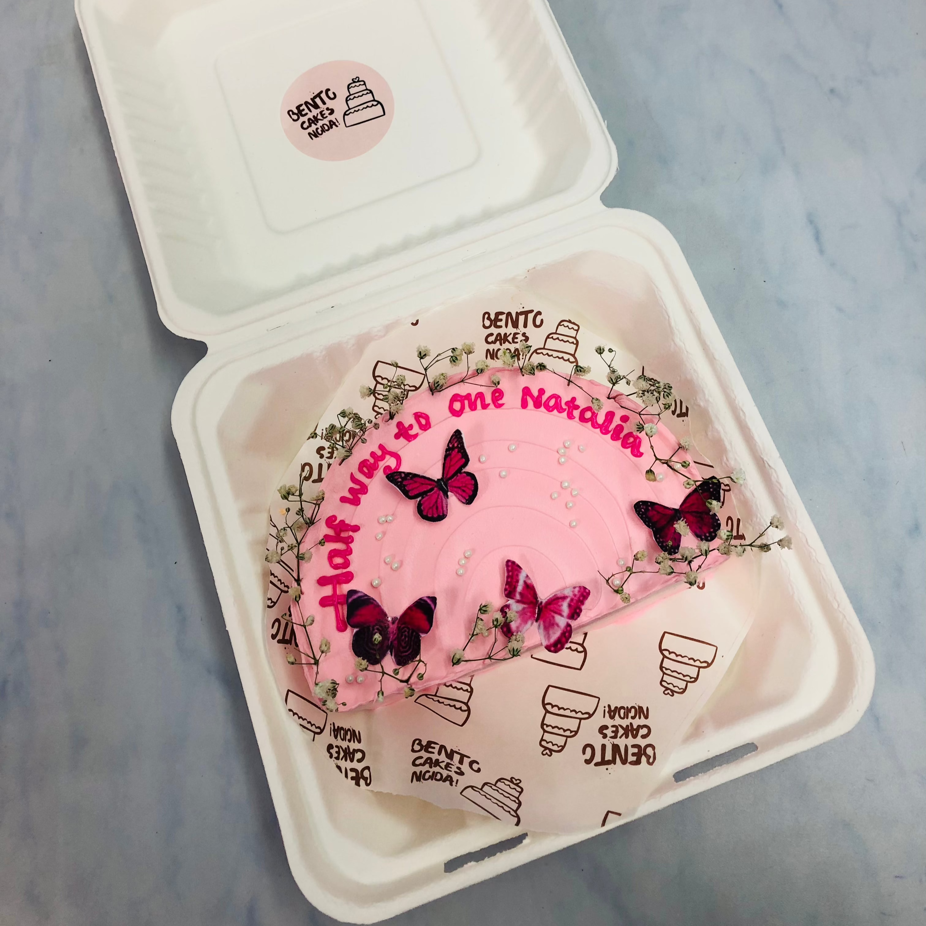 A baby pink half shape cake for 6 months baby birthday and is decorated with pink butterflies and florals.