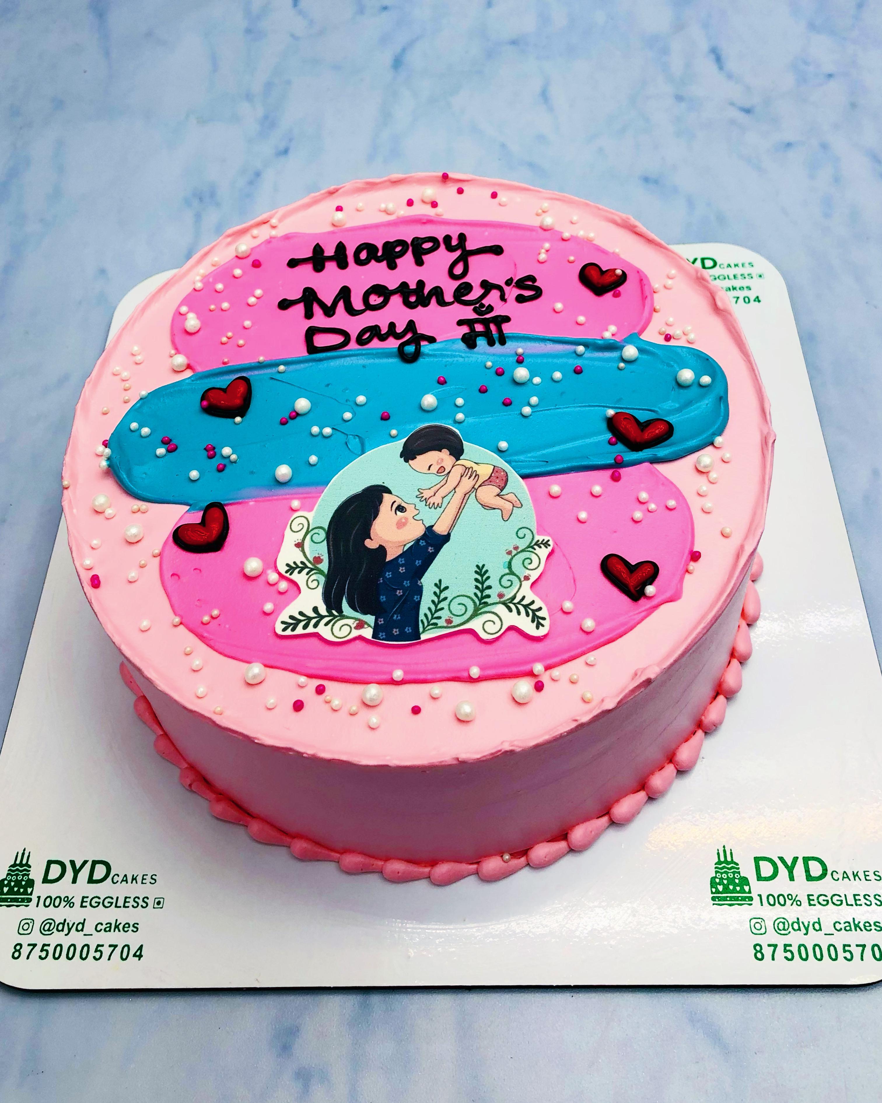 A pink cake with blue pink shades and a mothers baby sticker on it for mother's day occasion.