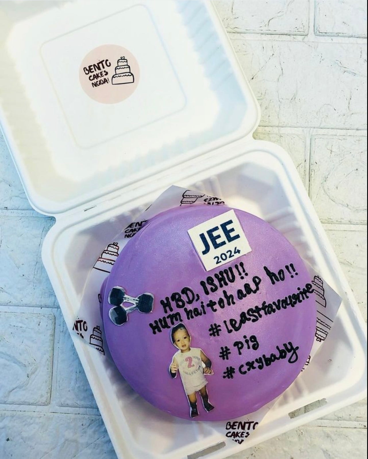 A purple bento cake with a baby boy print and a text written with black icing.