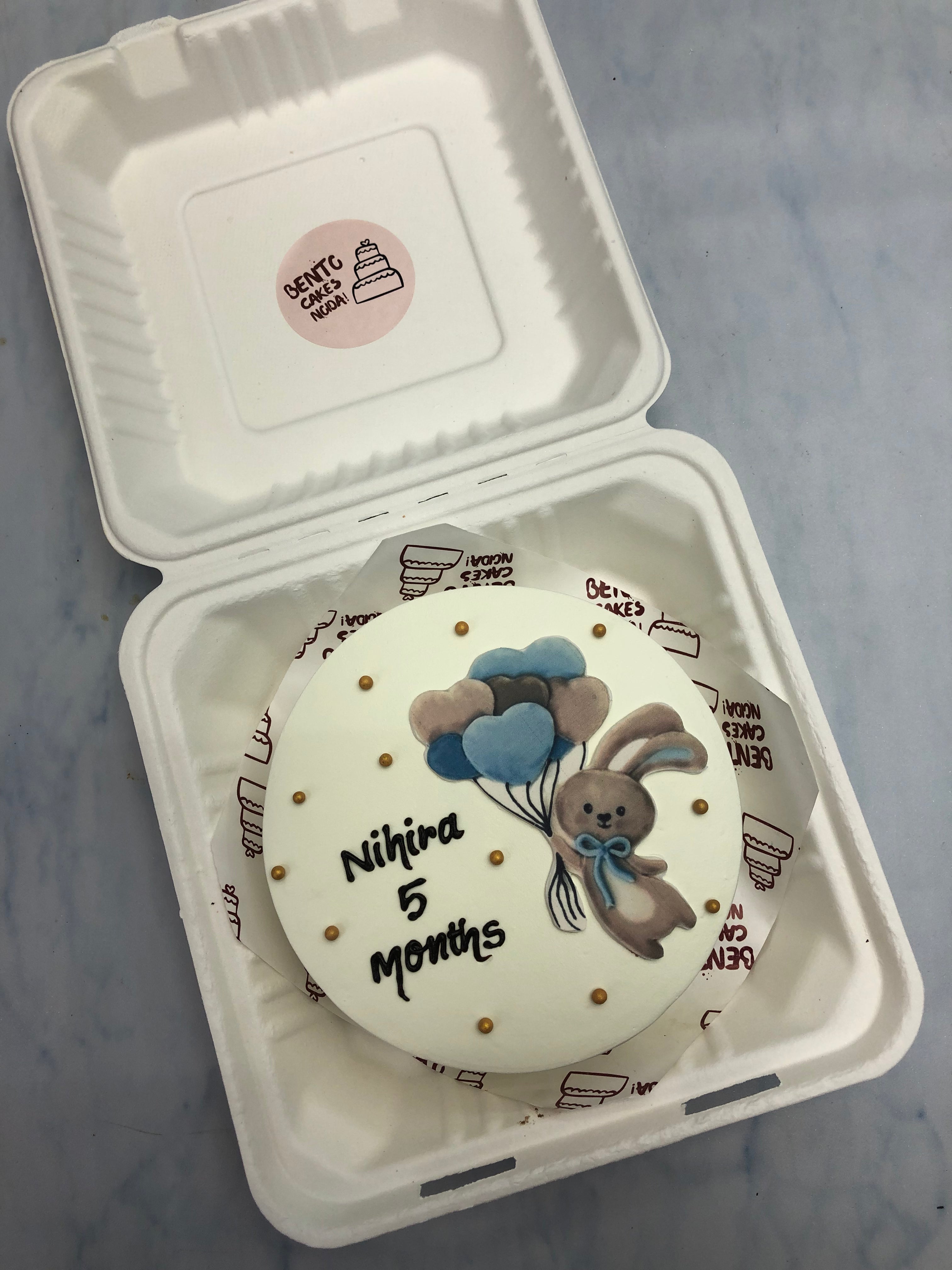 A white cake with cute rabbit taken balloons in hand and decorated with golden sprikles.