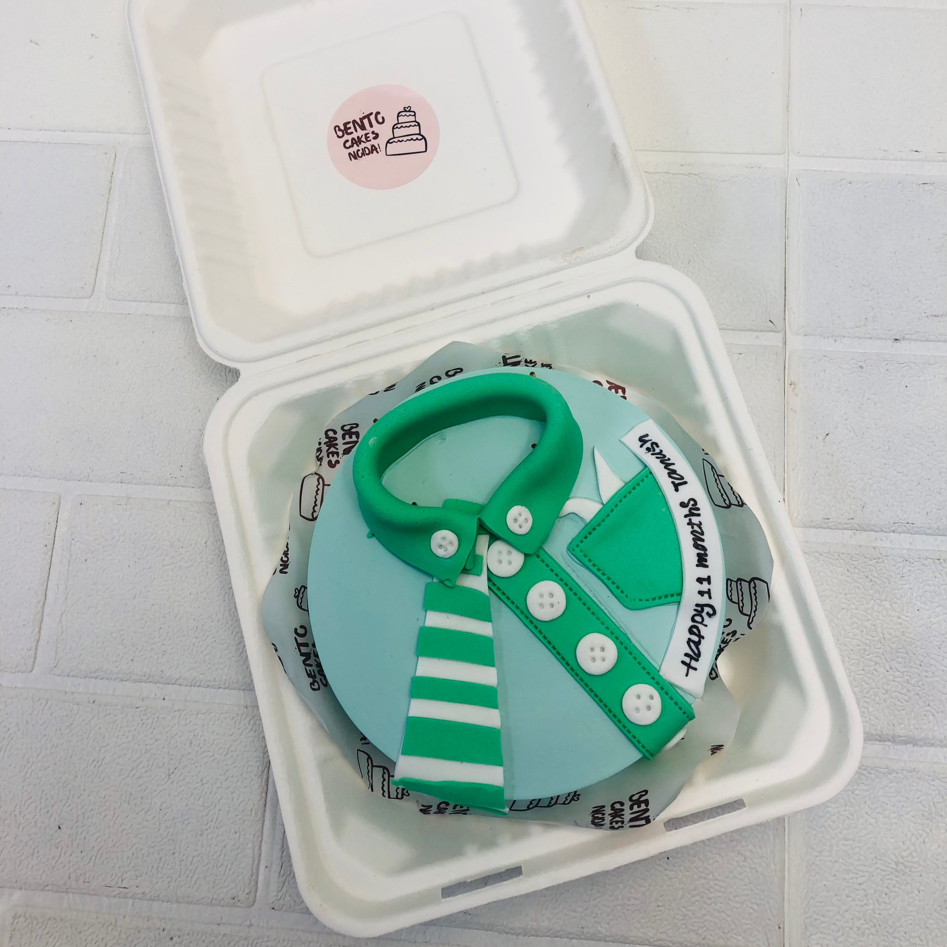 A light blue cake with baby shirt design with fondant.