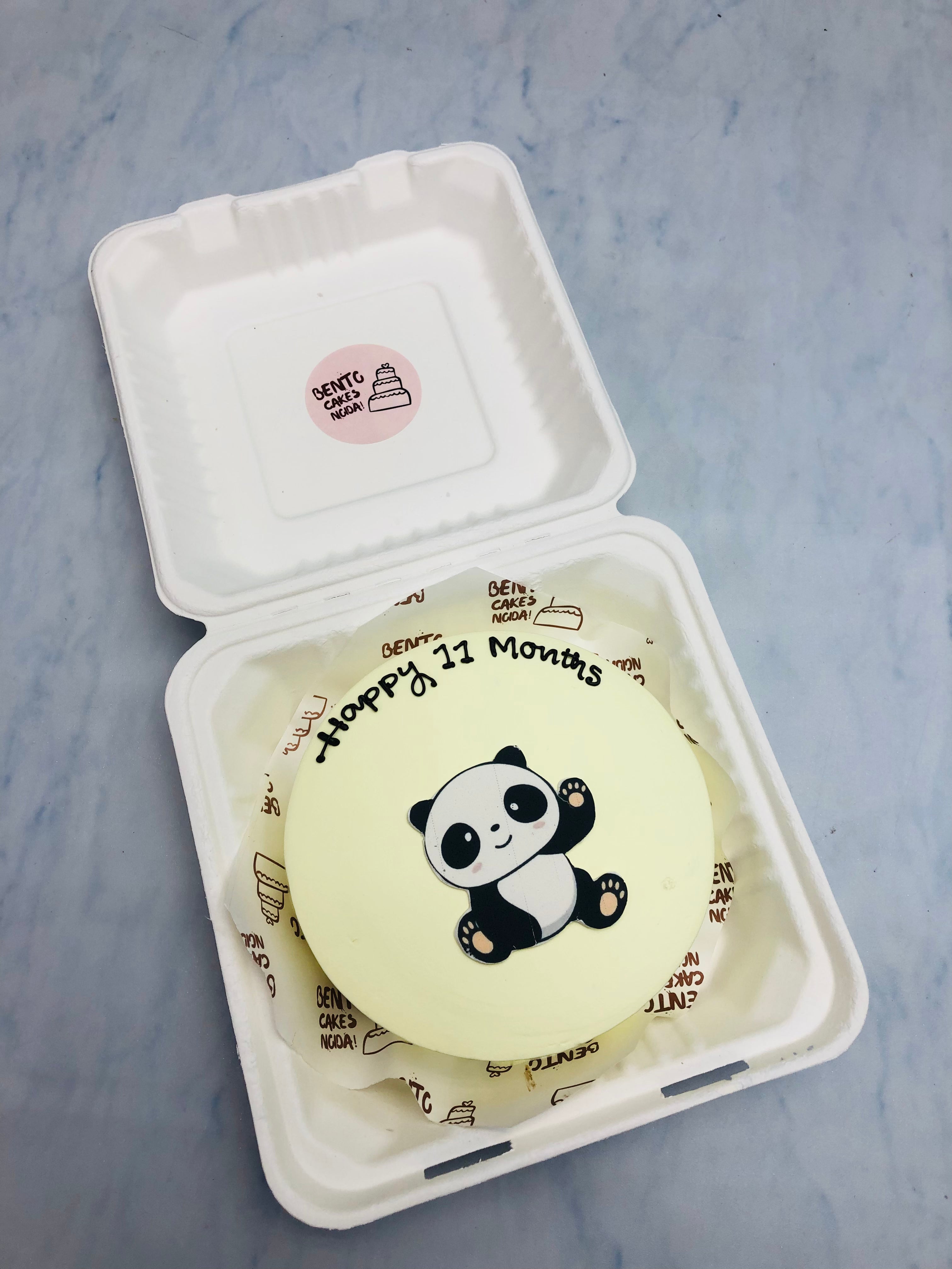 A offwhite cake with a cute bear print on cake and a "Happy 11 Months" text written with black color.