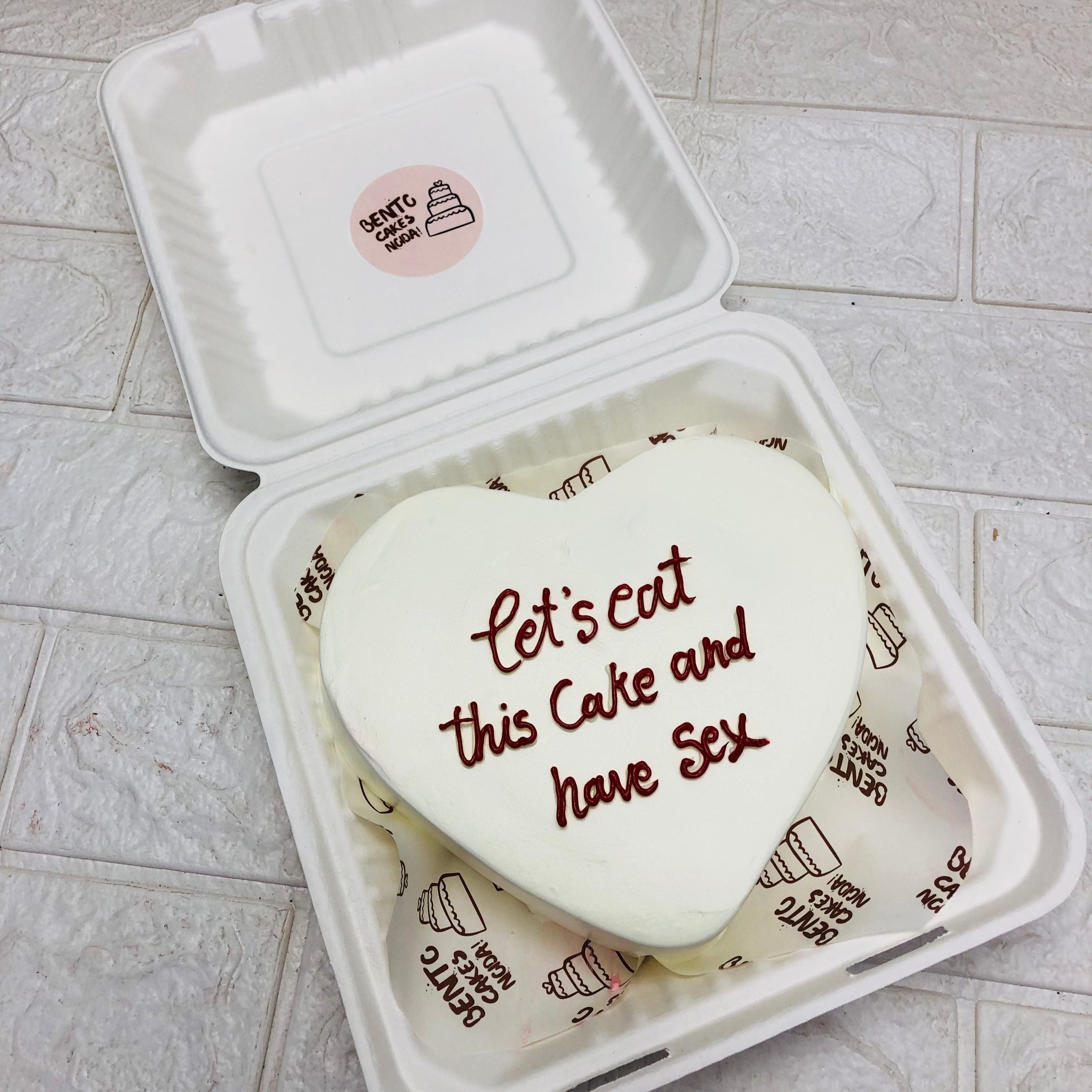 A heart-shaped cake adorned with the phrase "let's eat this cake and have sex" in decorative icing.