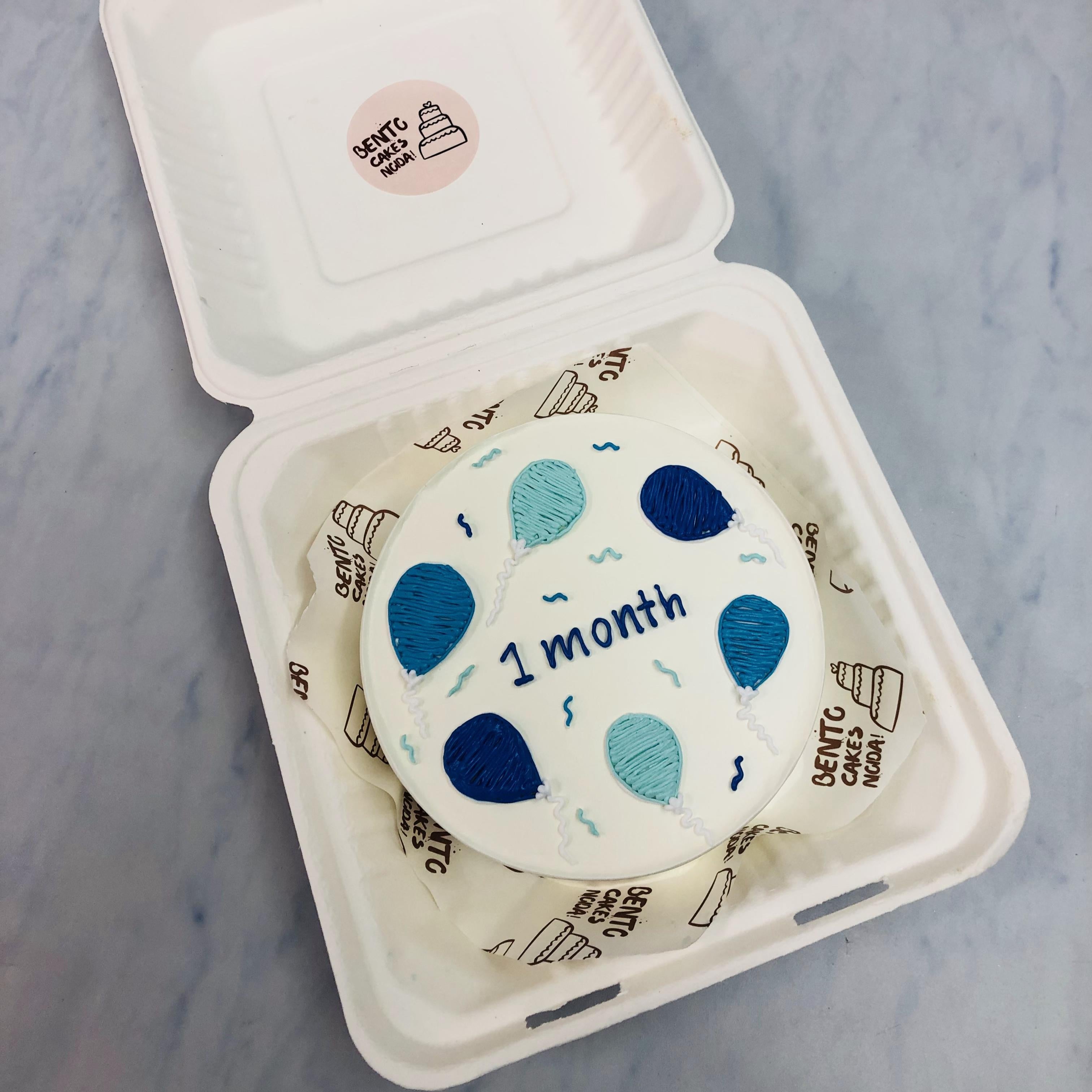 A white bento cake having blue and light blue balloon designs for 1 month baby.