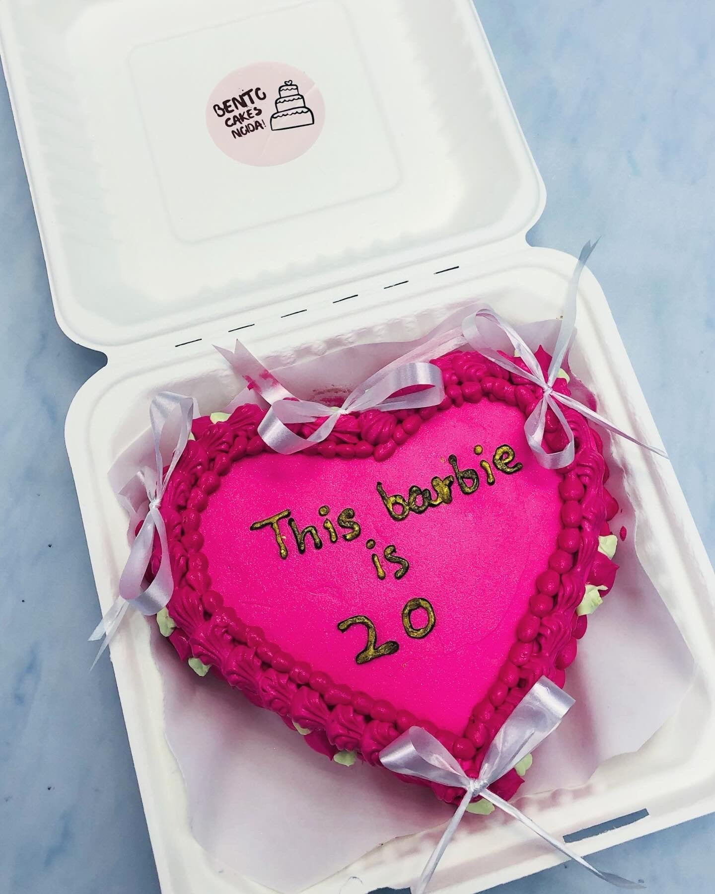 A dark pink icing cake decorated with white bows and pink creamy design on its boundary with a gloden text.