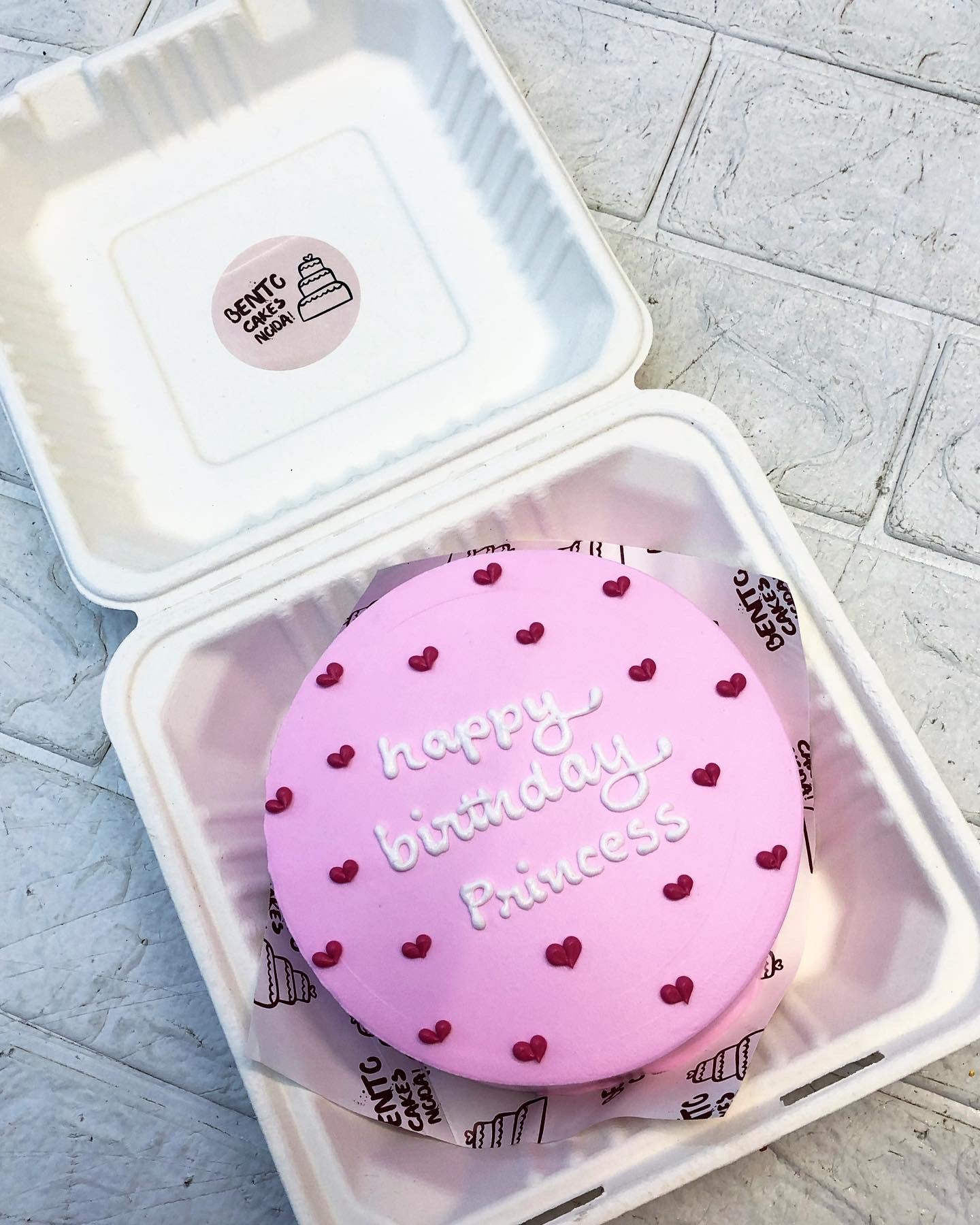 A pink frosting cake in a bento box decorated with dark pink hearts design with a "happy bitrthday Princess" text written with white icing on it.
