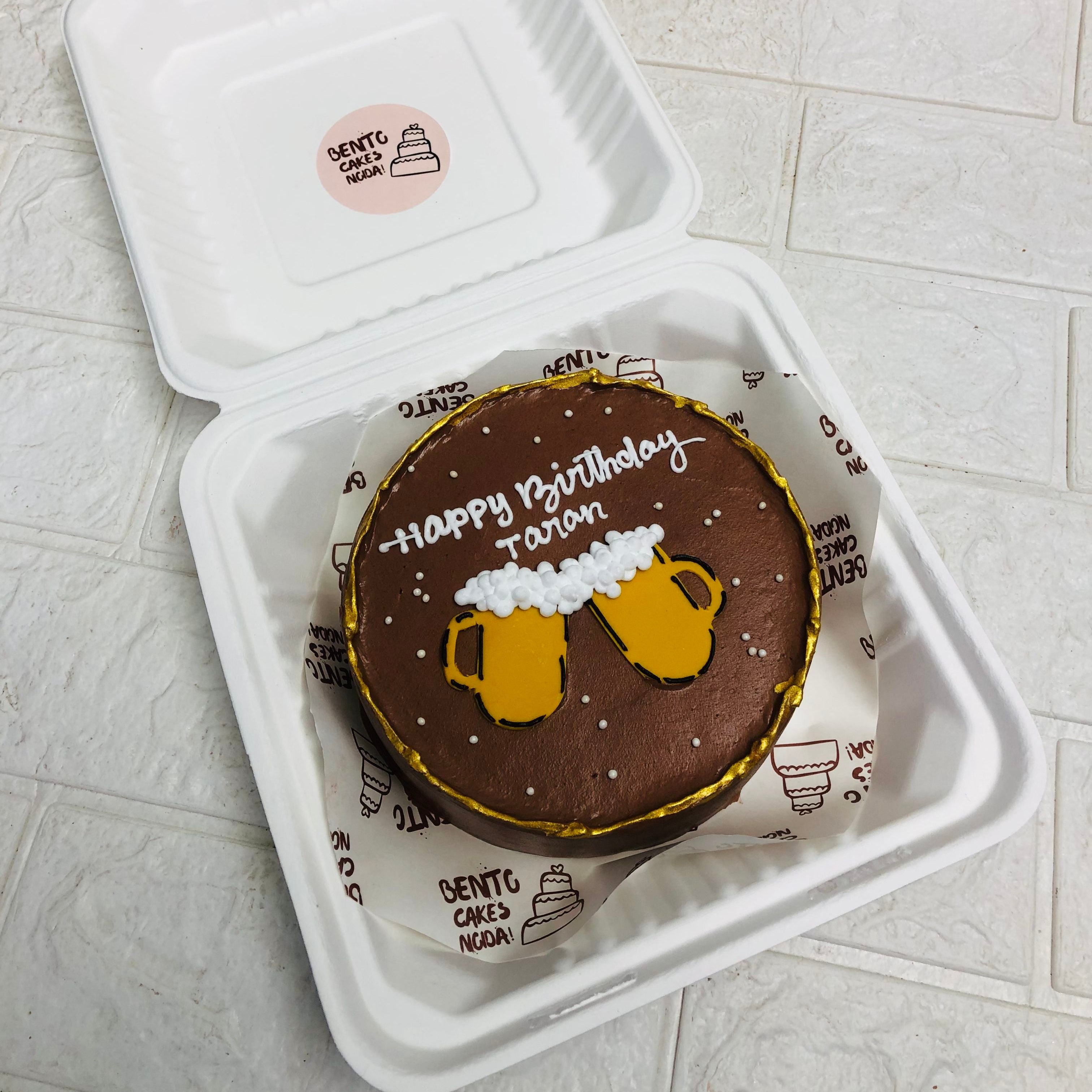 A cake placed in a box, adorned with two beer mugs on top, creating a festive and celebratory presentation.