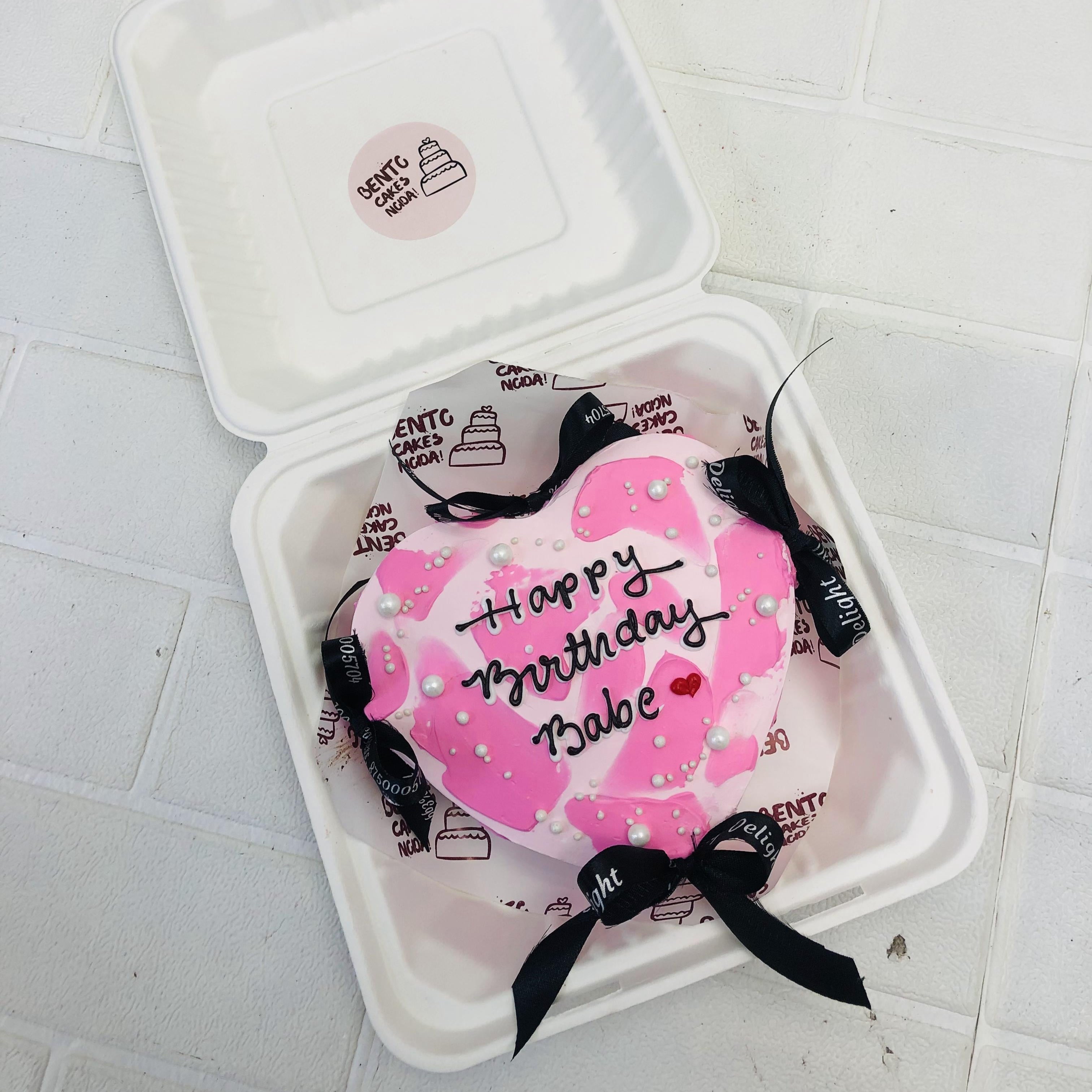 A Beautiful Heart shape bento cake with white and pink shades and decorated with black bows.