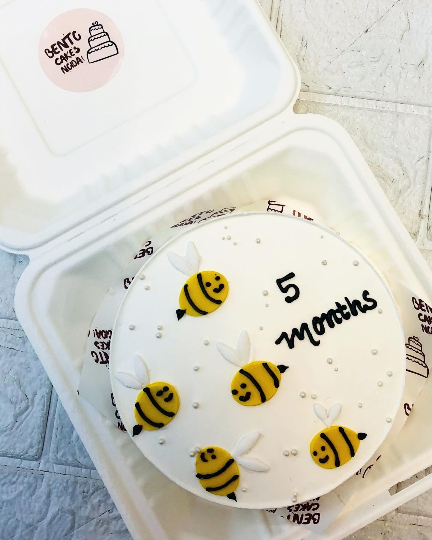 A white bento cake is designed with yellow bees and silver sprinkles on it.
