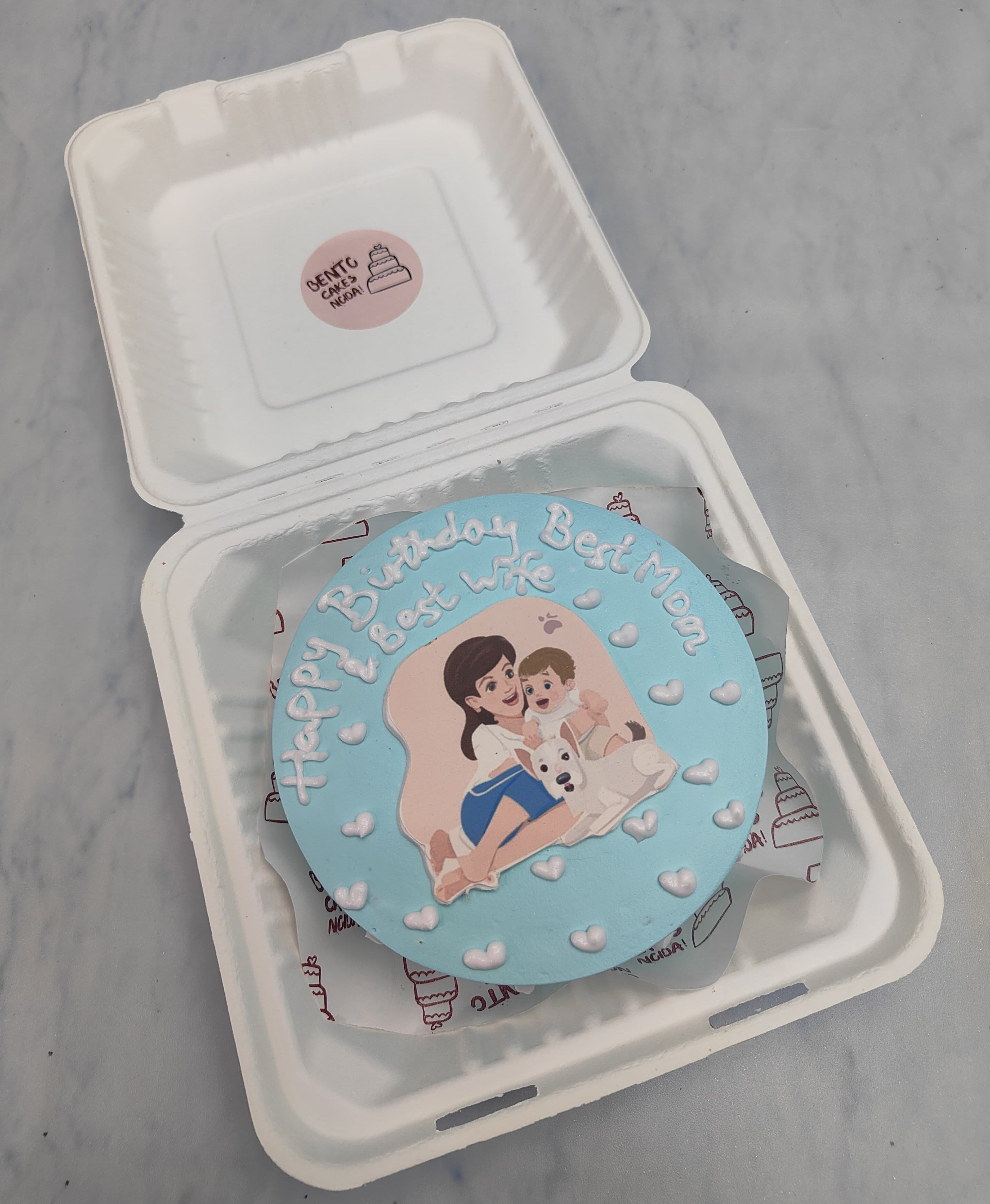 A light blue bento cake with a mom and baby print on it with her pet puppy. The cake shows best mom and wife emotion.