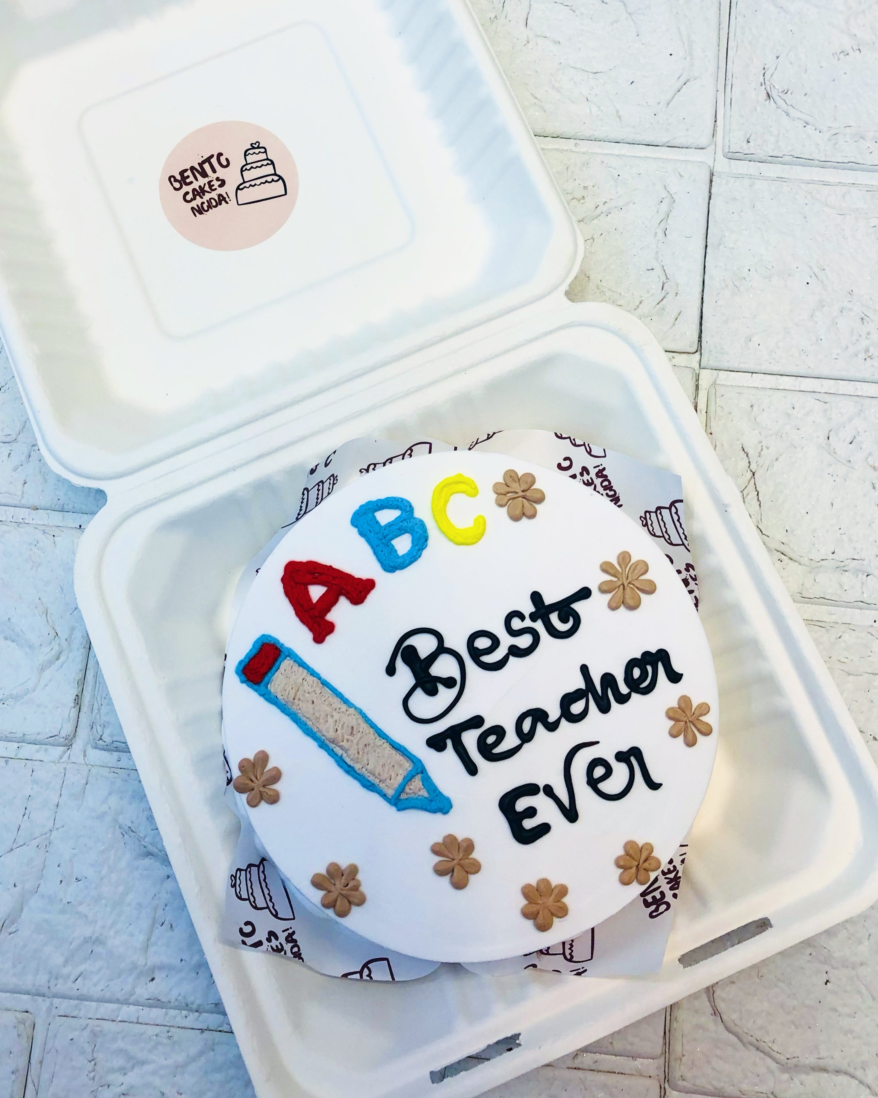 A white bento cake is designed on a theme of Best Teacher Ever with floral and Pencil design.