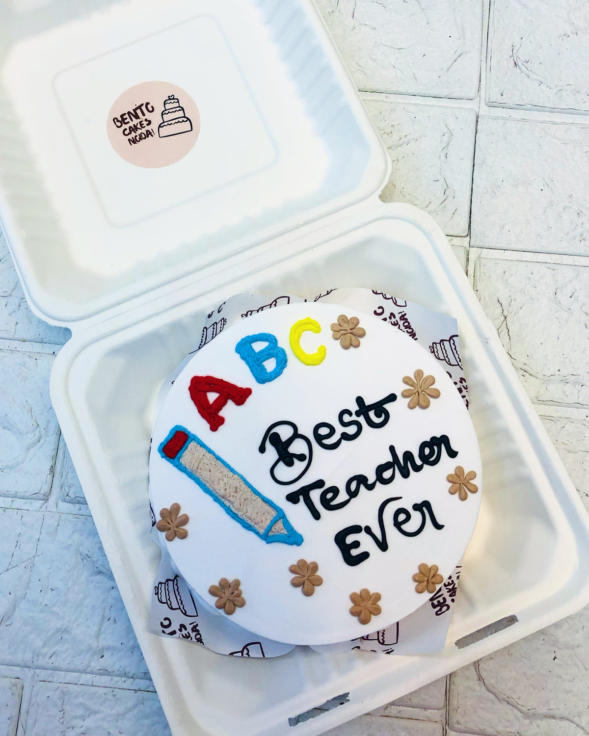 A white bento cake is designed on a theme of Best Teacher Ever with floral and Pencil design.