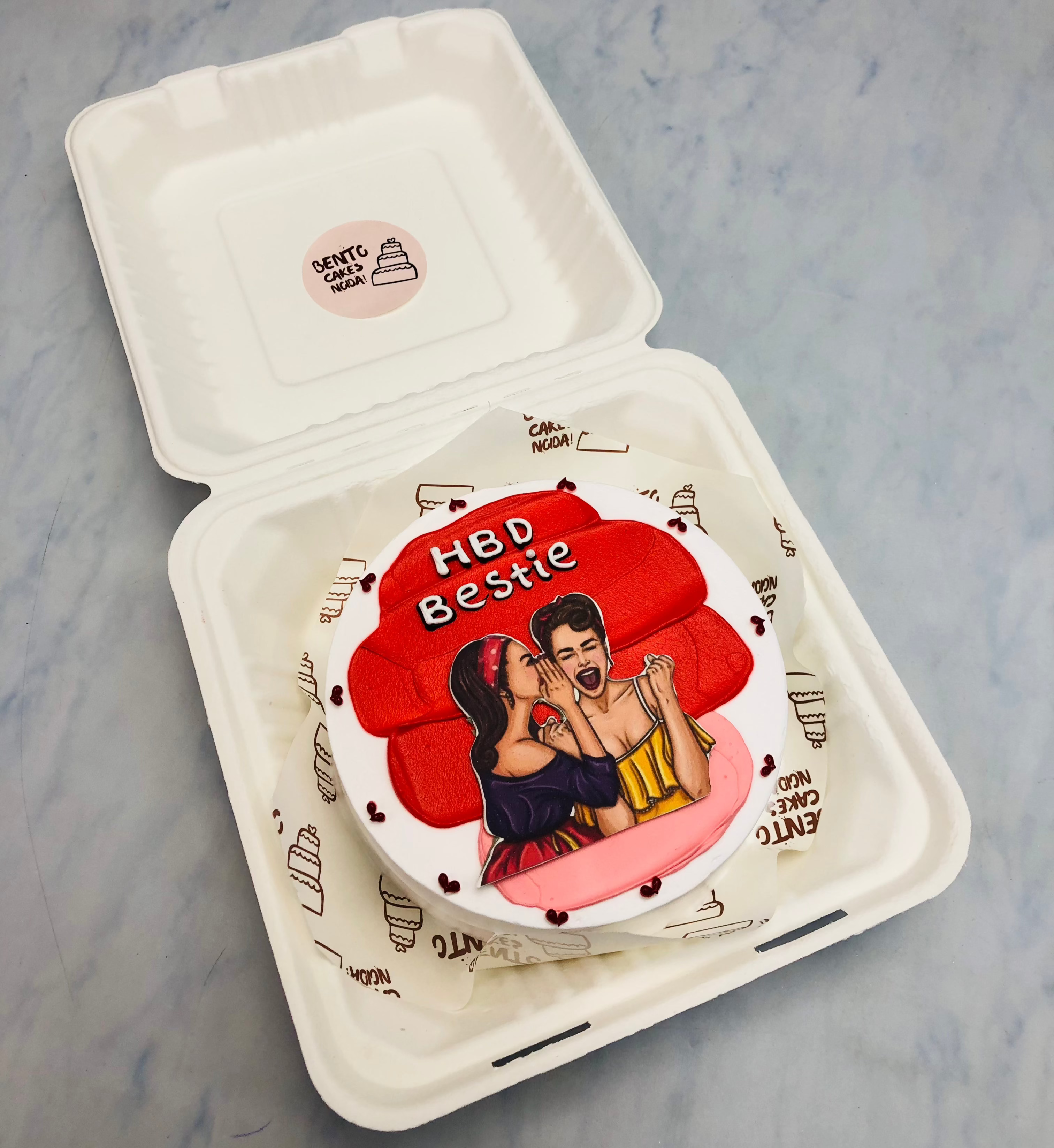 A white bento cake with red shades on top and two best friends talking to each other.
