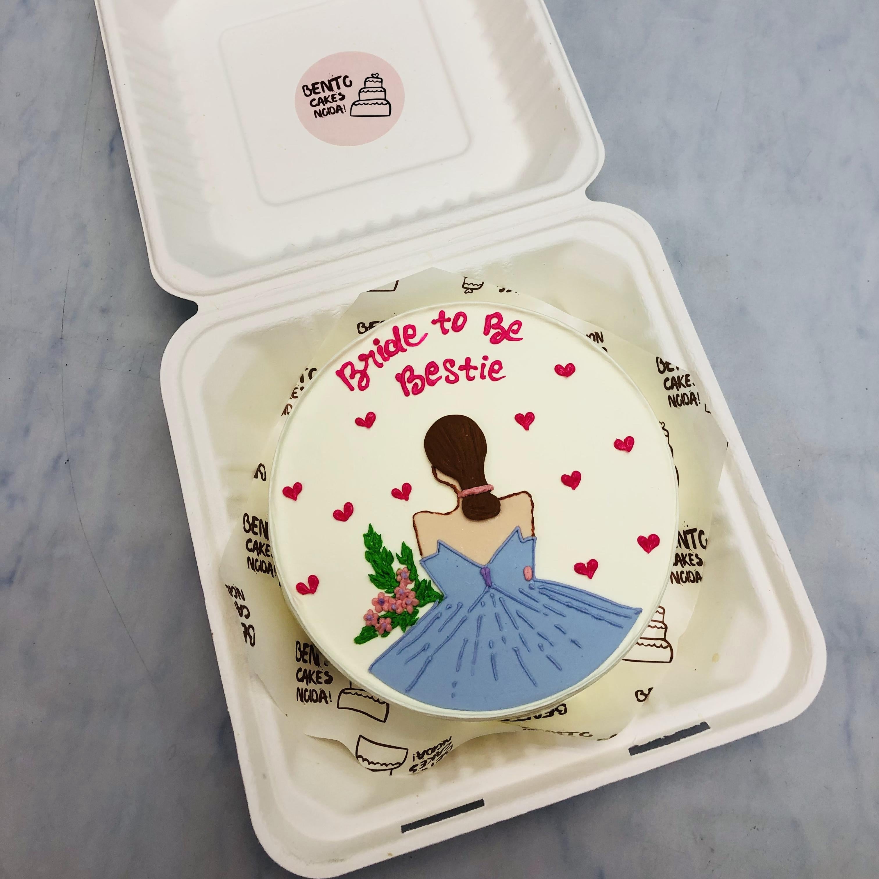 A pretty white bento cake with a bridal wearing blue dress with flowers in hand.