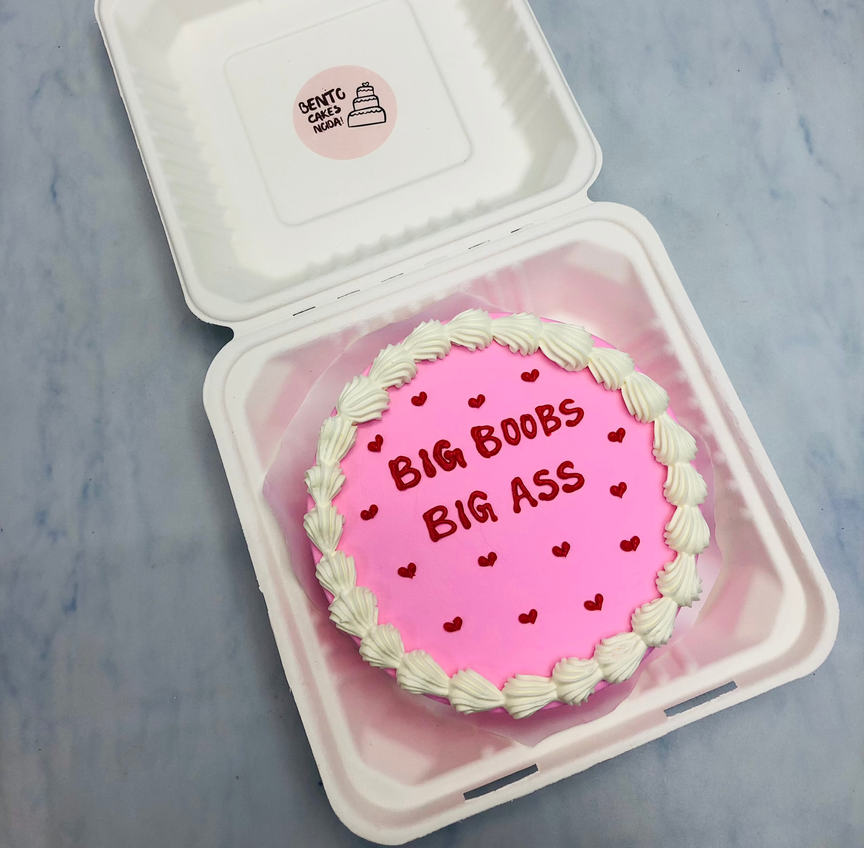 A light pink bento cake with white truffle designs on it's boundary and a bachelor text written with red color.