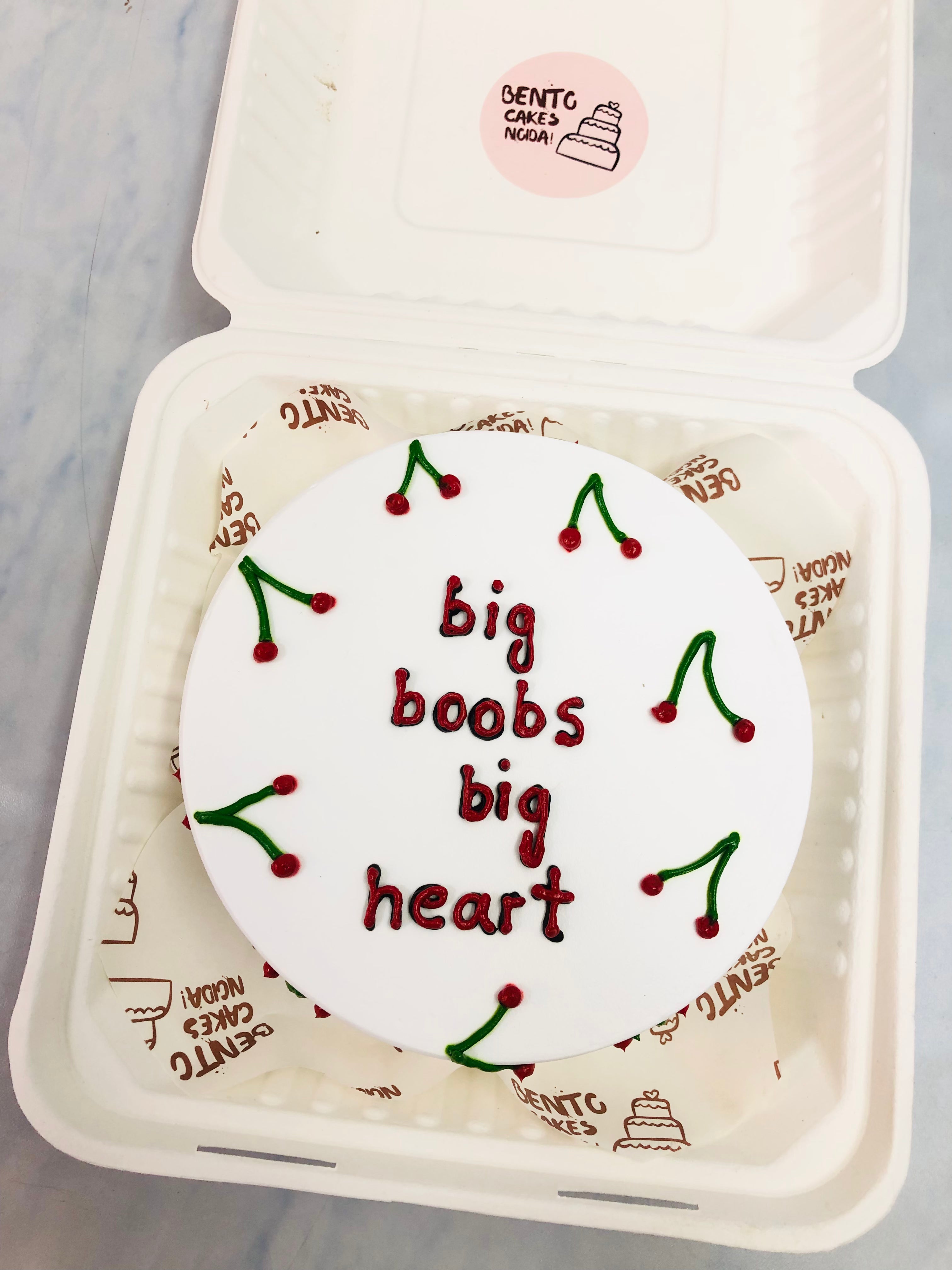 A white bento cake with berries design and a bachelor text "big boobs big heart" written with green red icing.