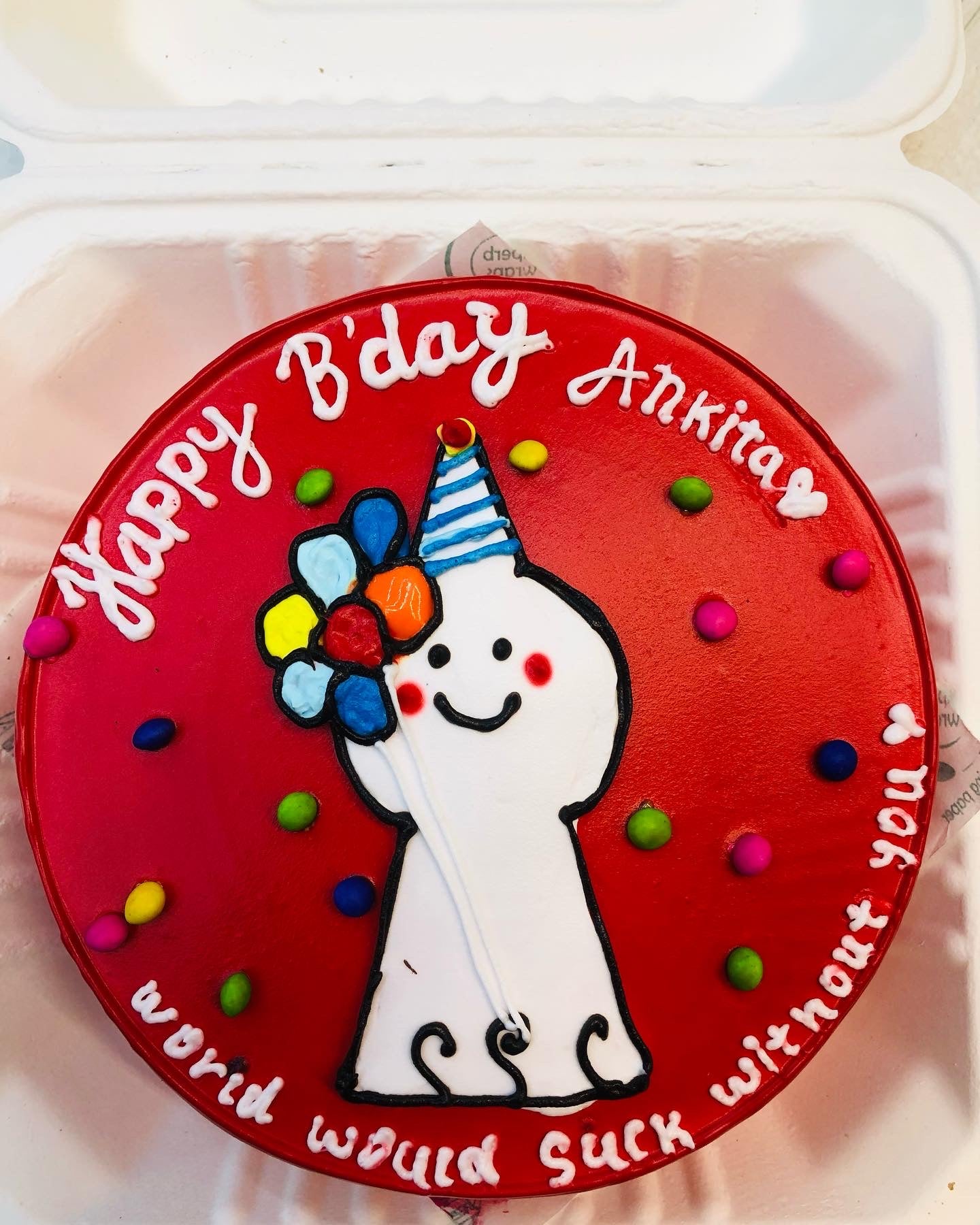 A vibrant red color cake is decorated with a cute cartoon design having a bundle of balloons and two texts written with white icing on it.