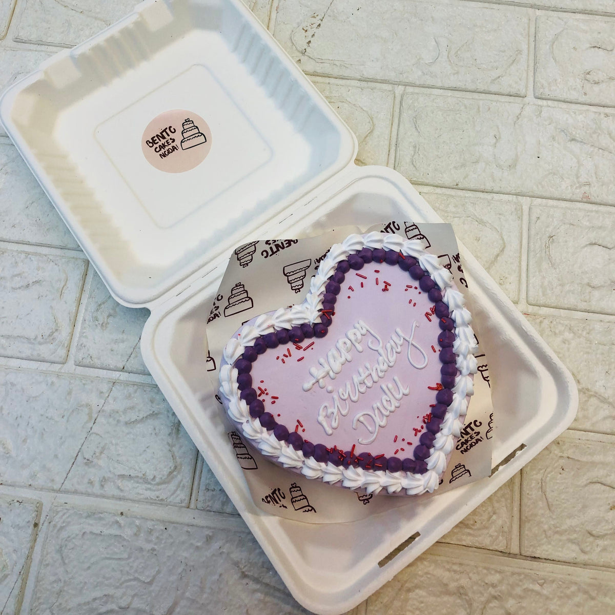 A whte heart shape cake decorated with blue and white boundaries.