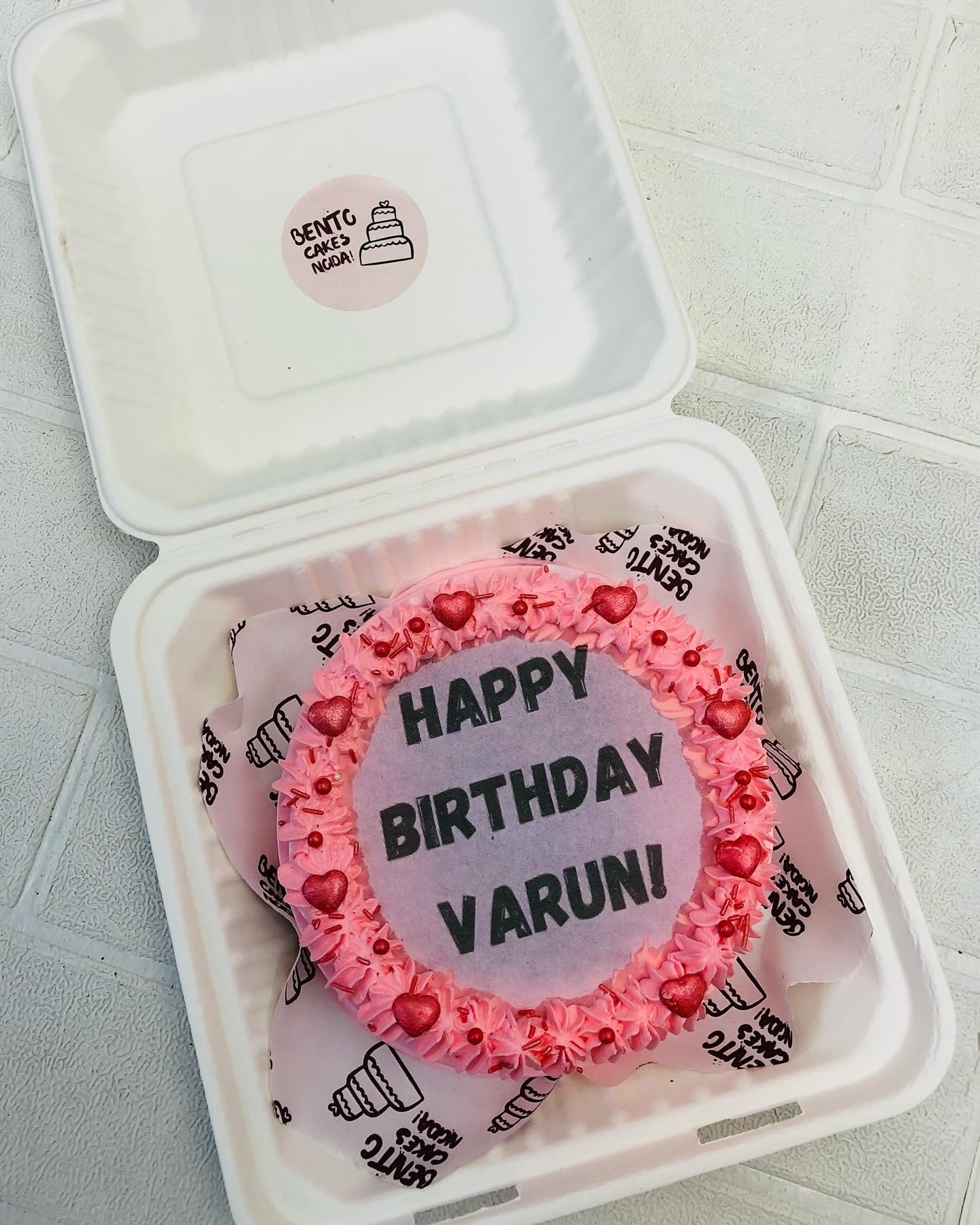 A shiny pink fire bento cake with a "Happy Birthday Varuni" text written on fire paper.