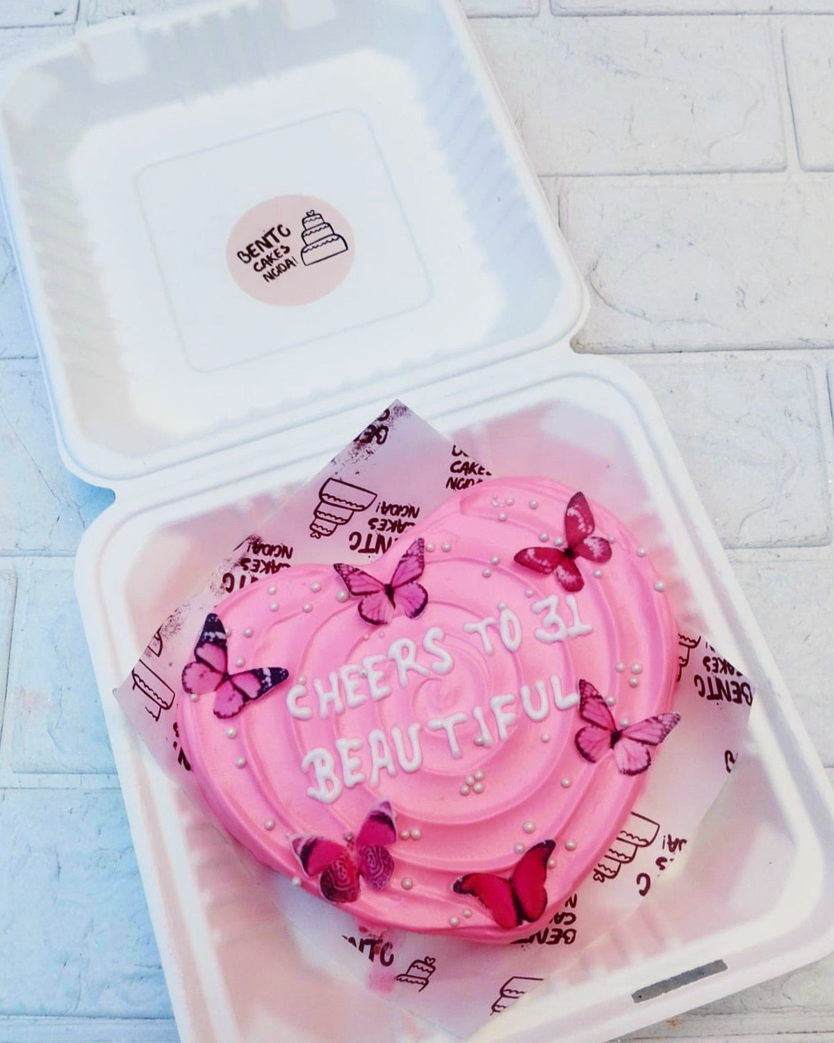 A light pink heart shape bento cake with pink butterflies on it and decorsted with pink sprinkles and a loving text.