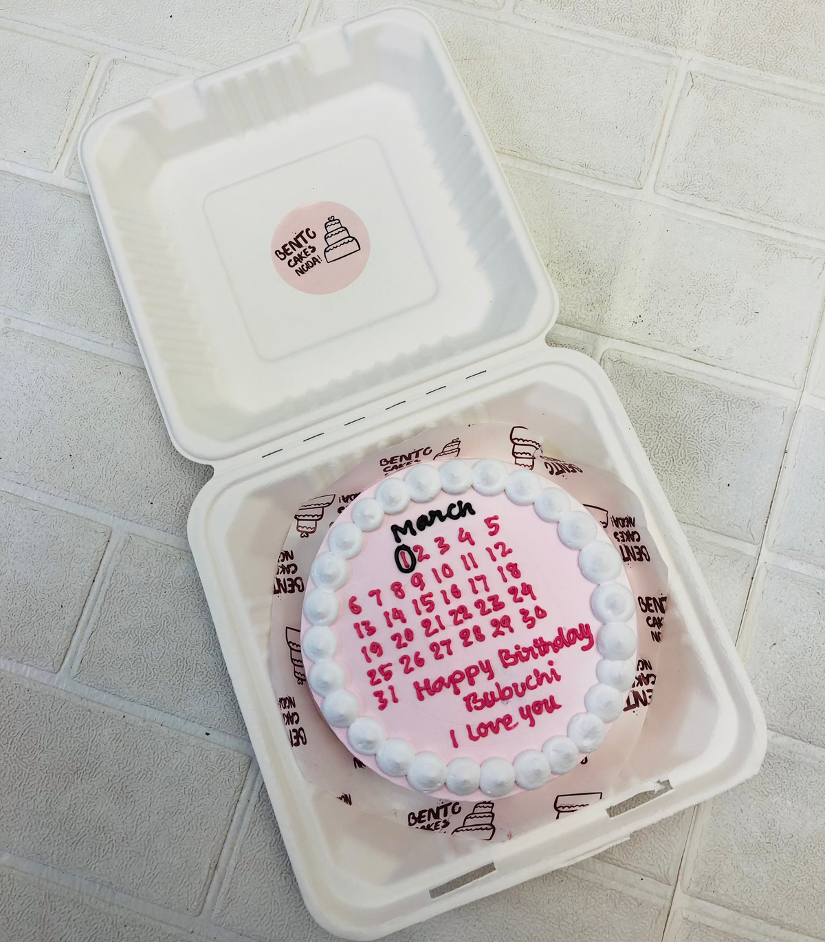A white calener design cake with pink text.