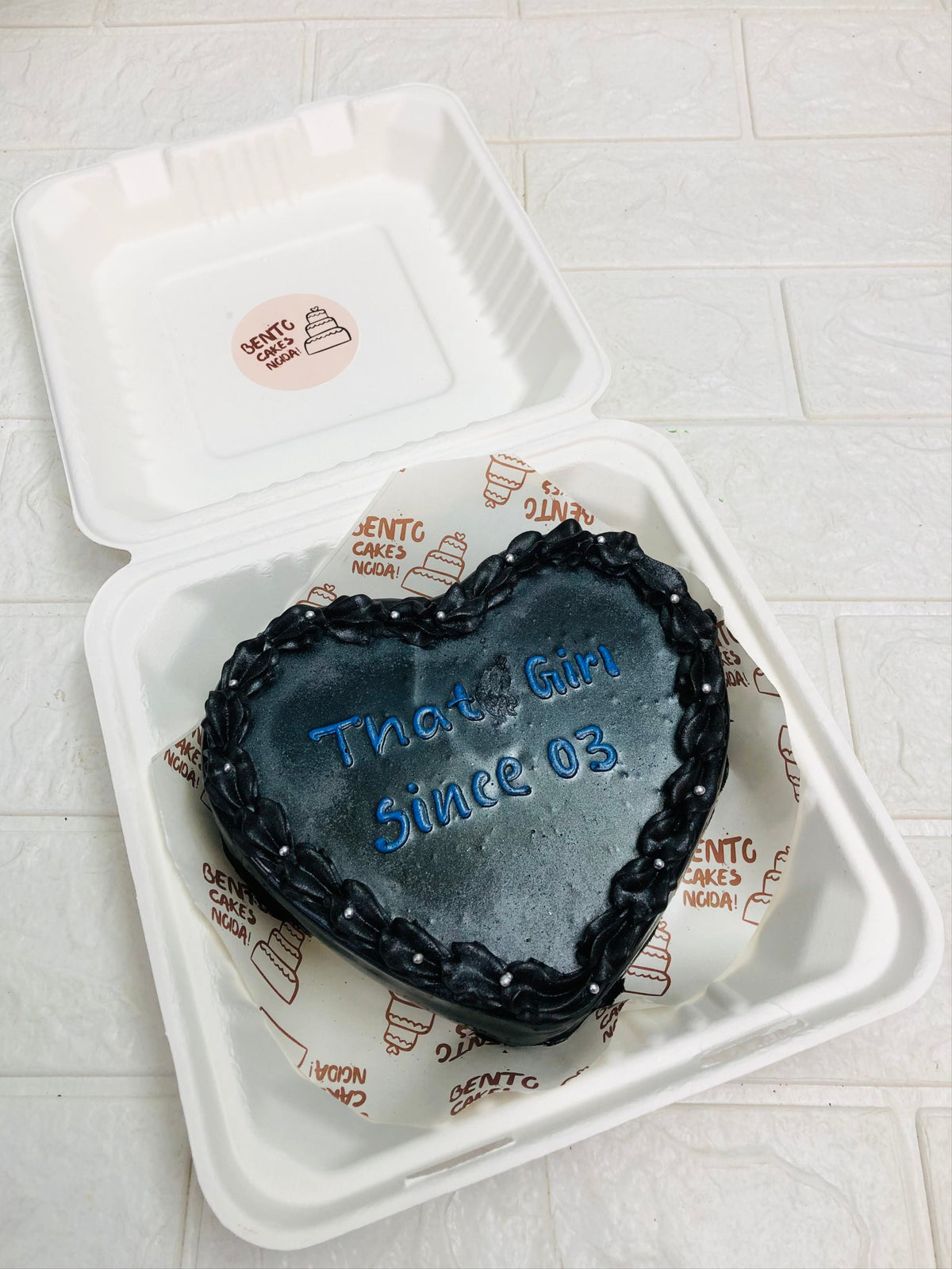 A shiney black chocolate cake designed in heart shape with a cute text on it.