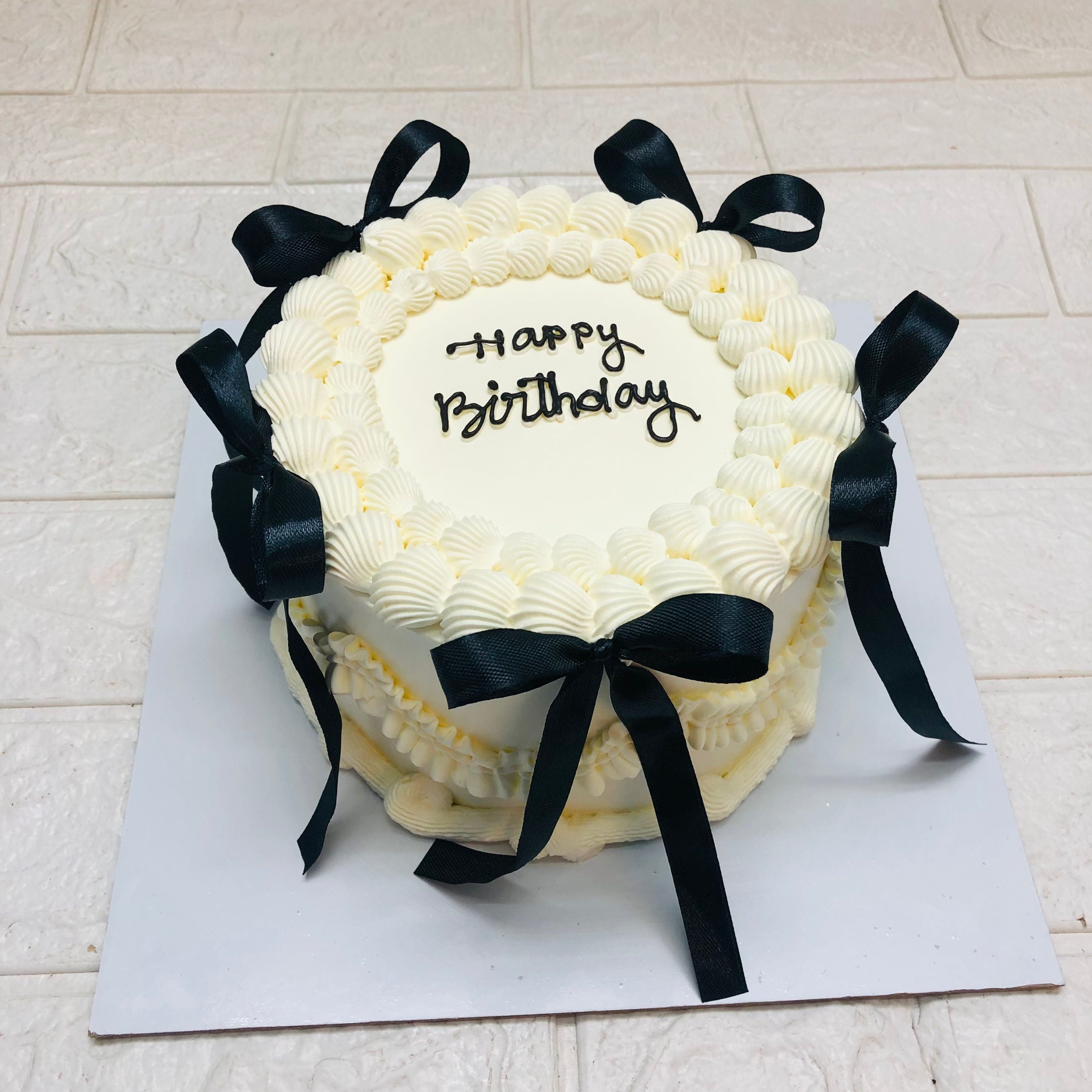 A festive birthday cake featuring elegant black ribbons and a joyful "Happy Birthday" inscription.