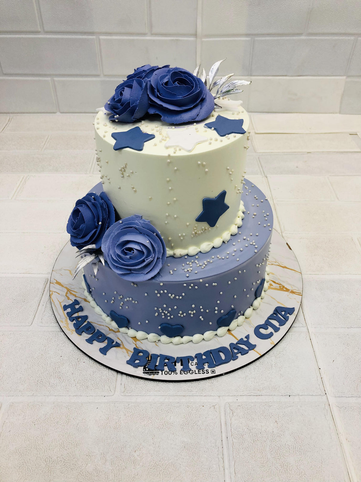 A 2 tier white and blue cake with blue creamy florals design for birthday celebration.