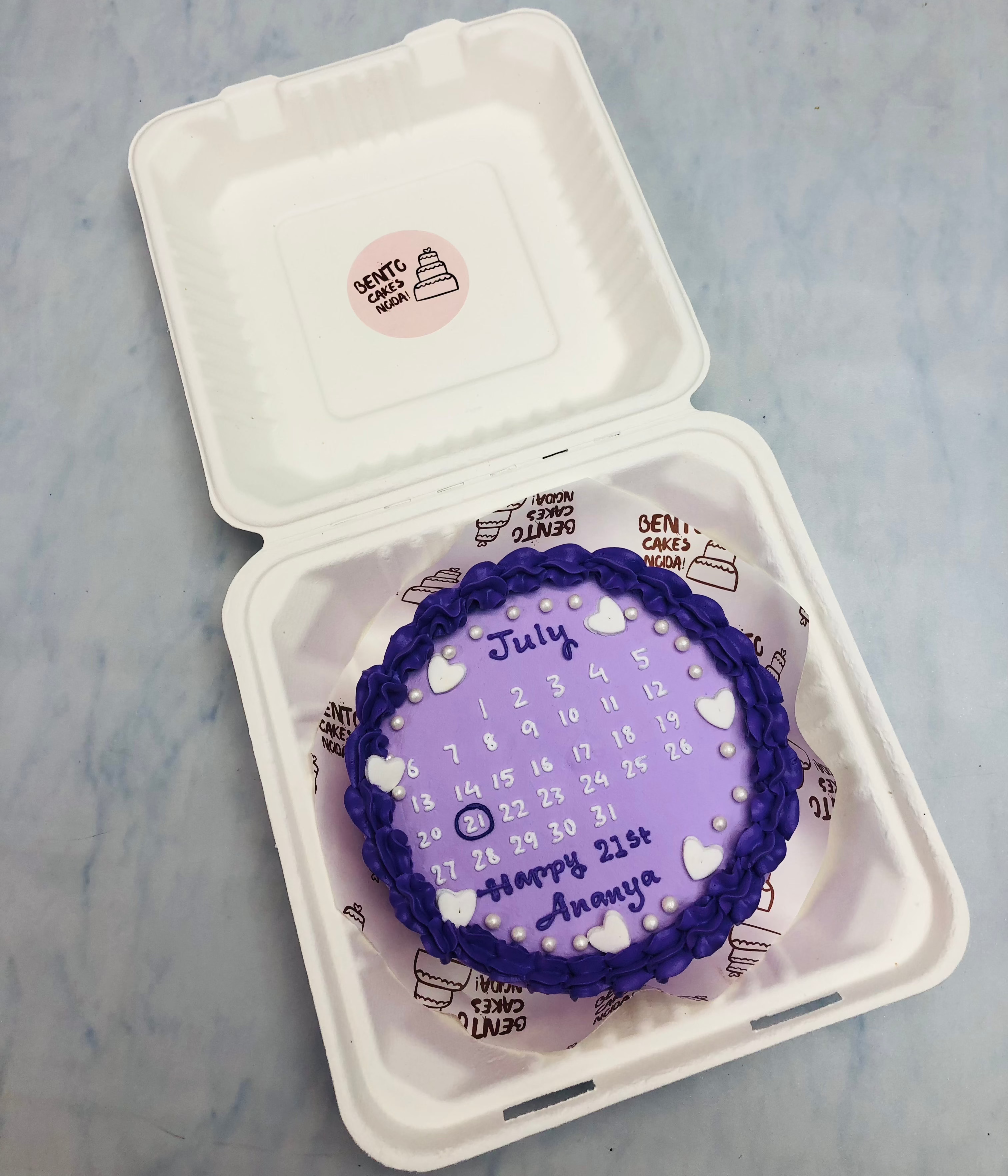 A blue calendar bento cake with little hearts on  it.