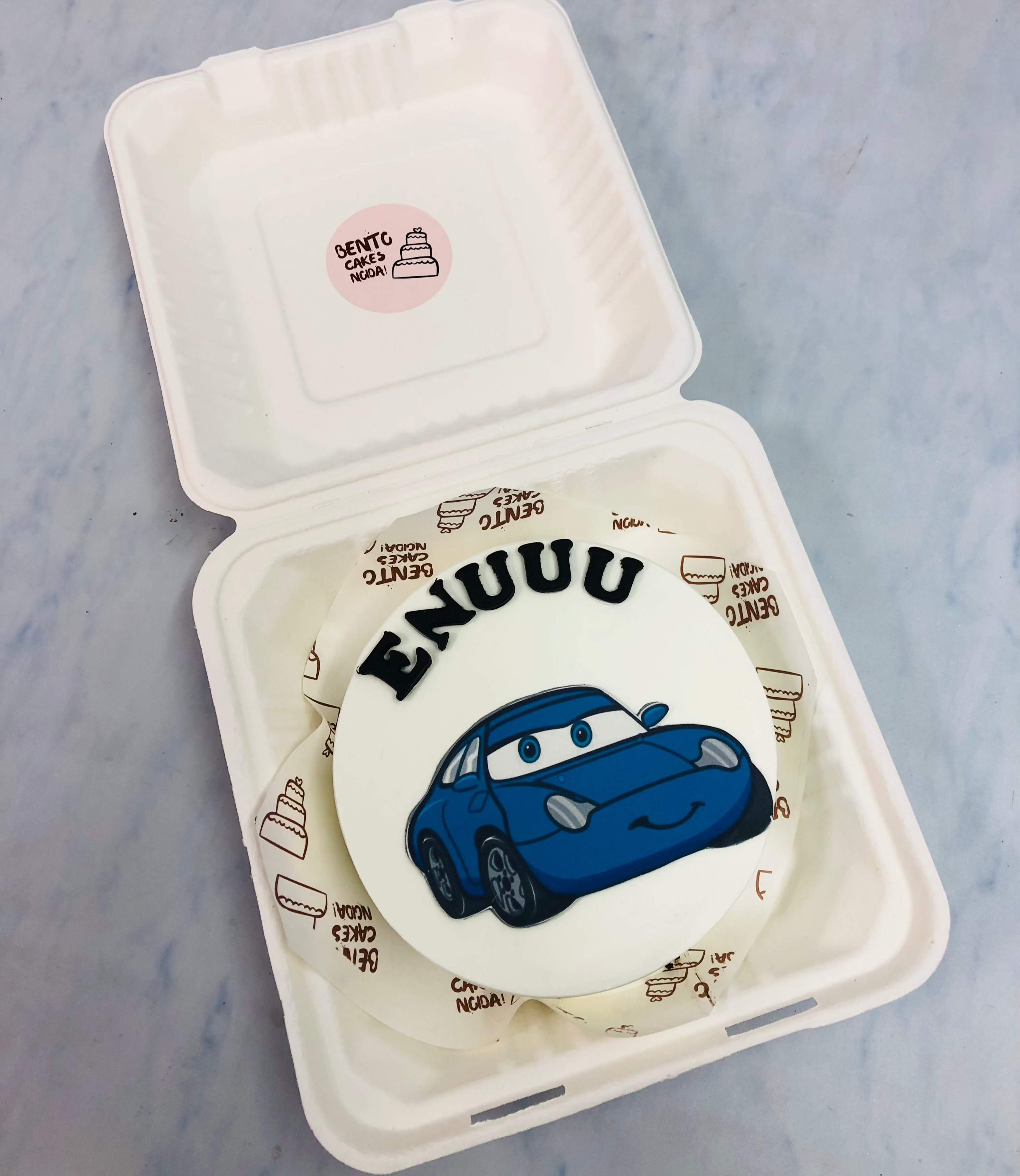 A white bento cake with a blue cartoon car print.