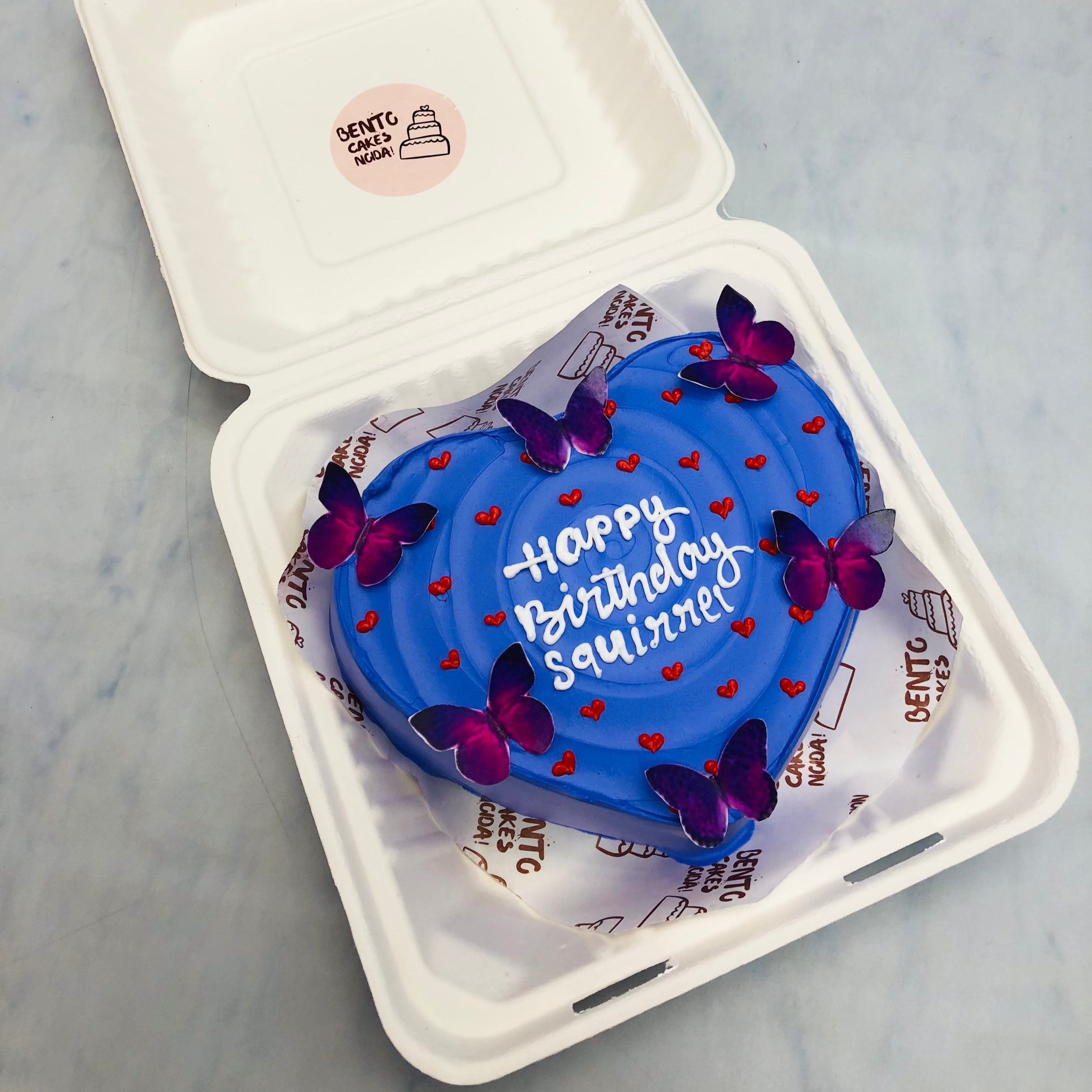 A dark blue heart shape aesthetic bento cake with purple butterflies and designed with little hearts design.