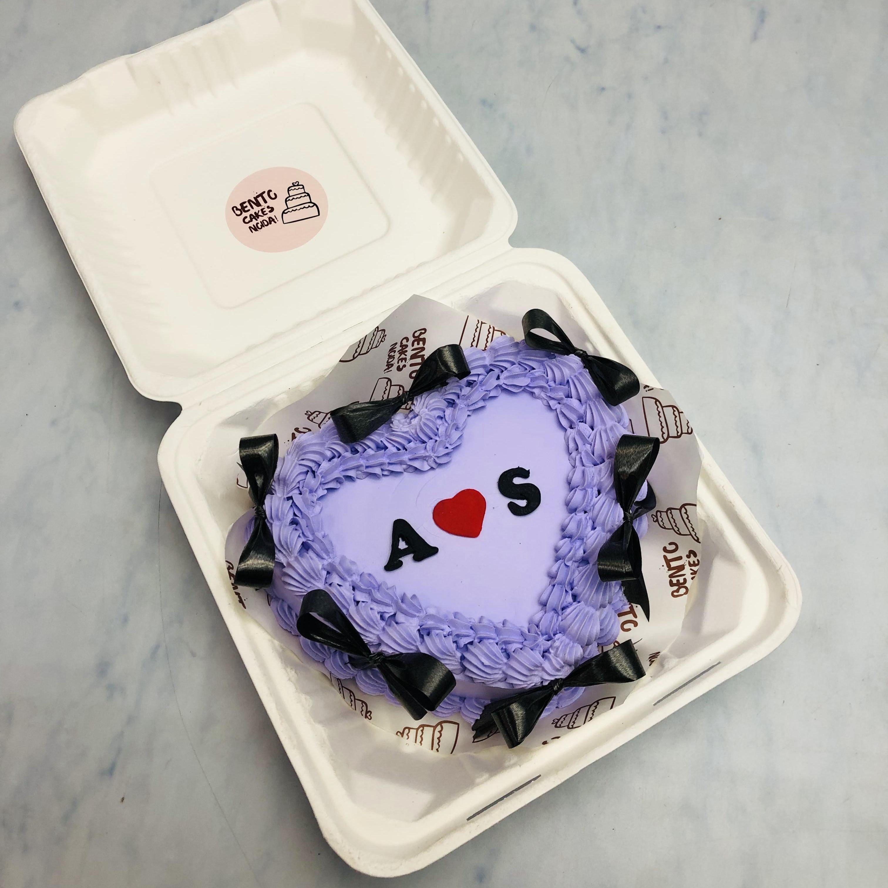 A blue color heart shape bento cake decorated with black bows and a ed fondent heart in the center with couple names.