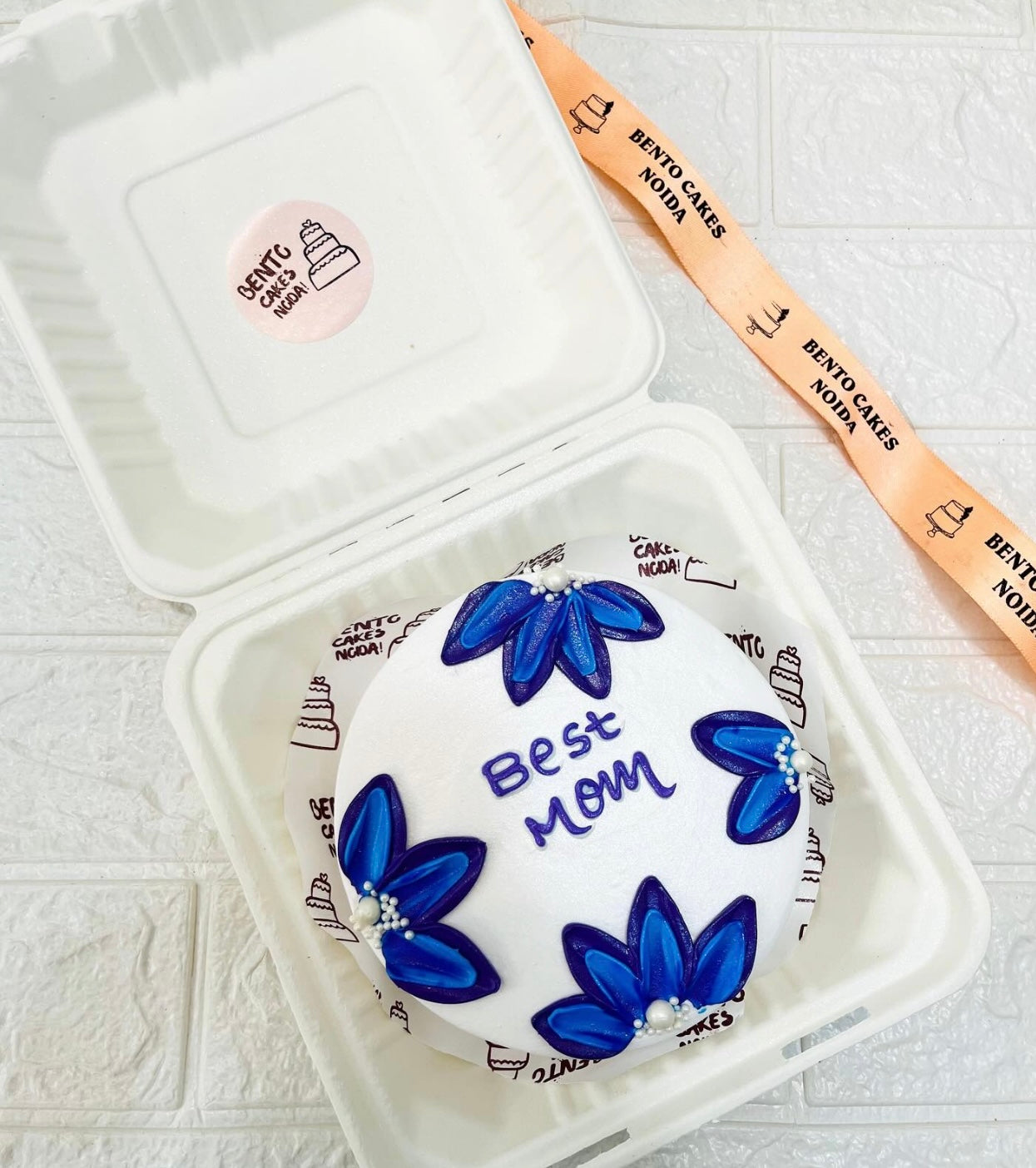 A white cake designed with aesthetic blue floral shape on it with a blue text for Mom.