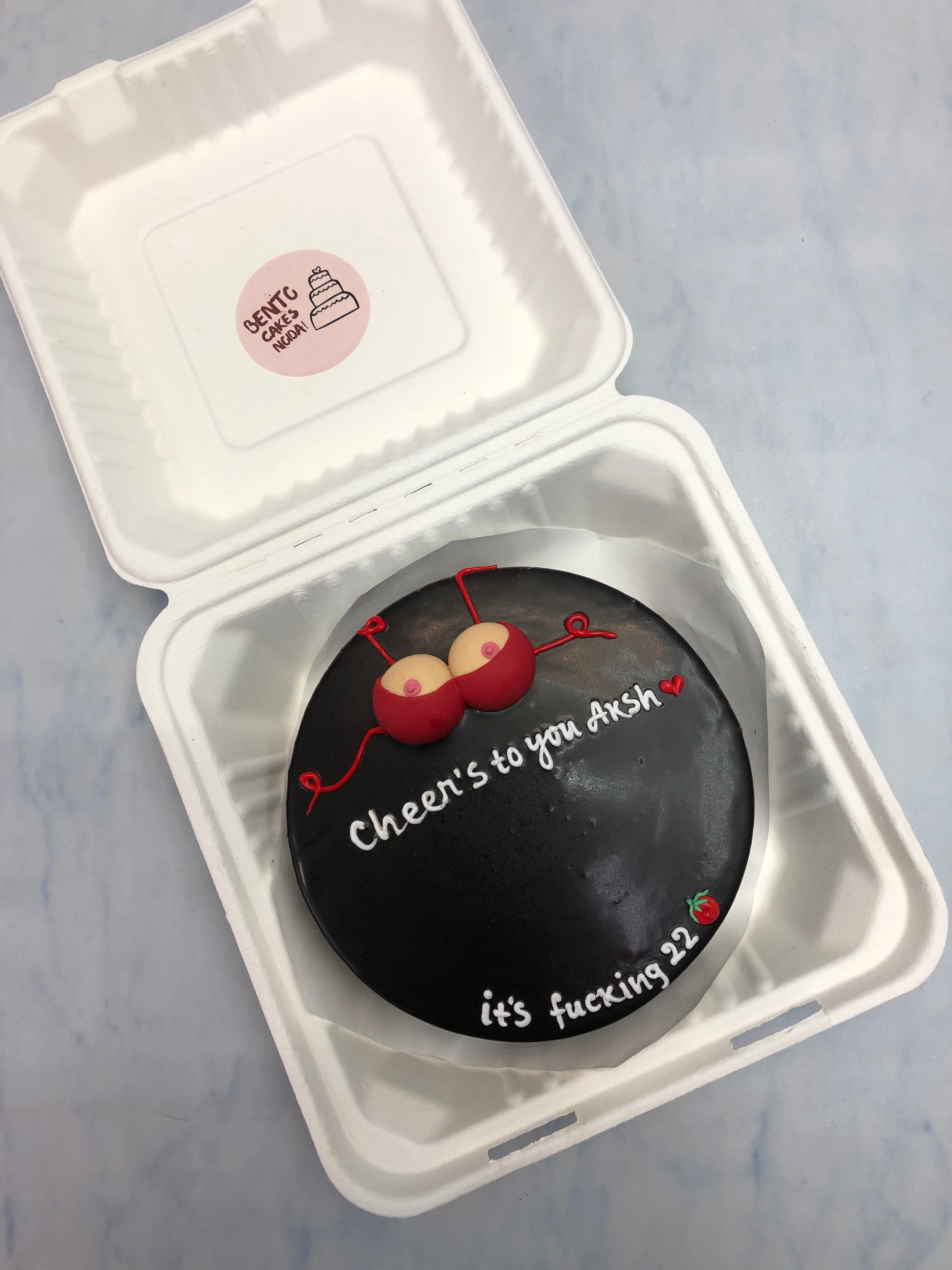A black bento cake with a boobs desin on it with red fondant on it.