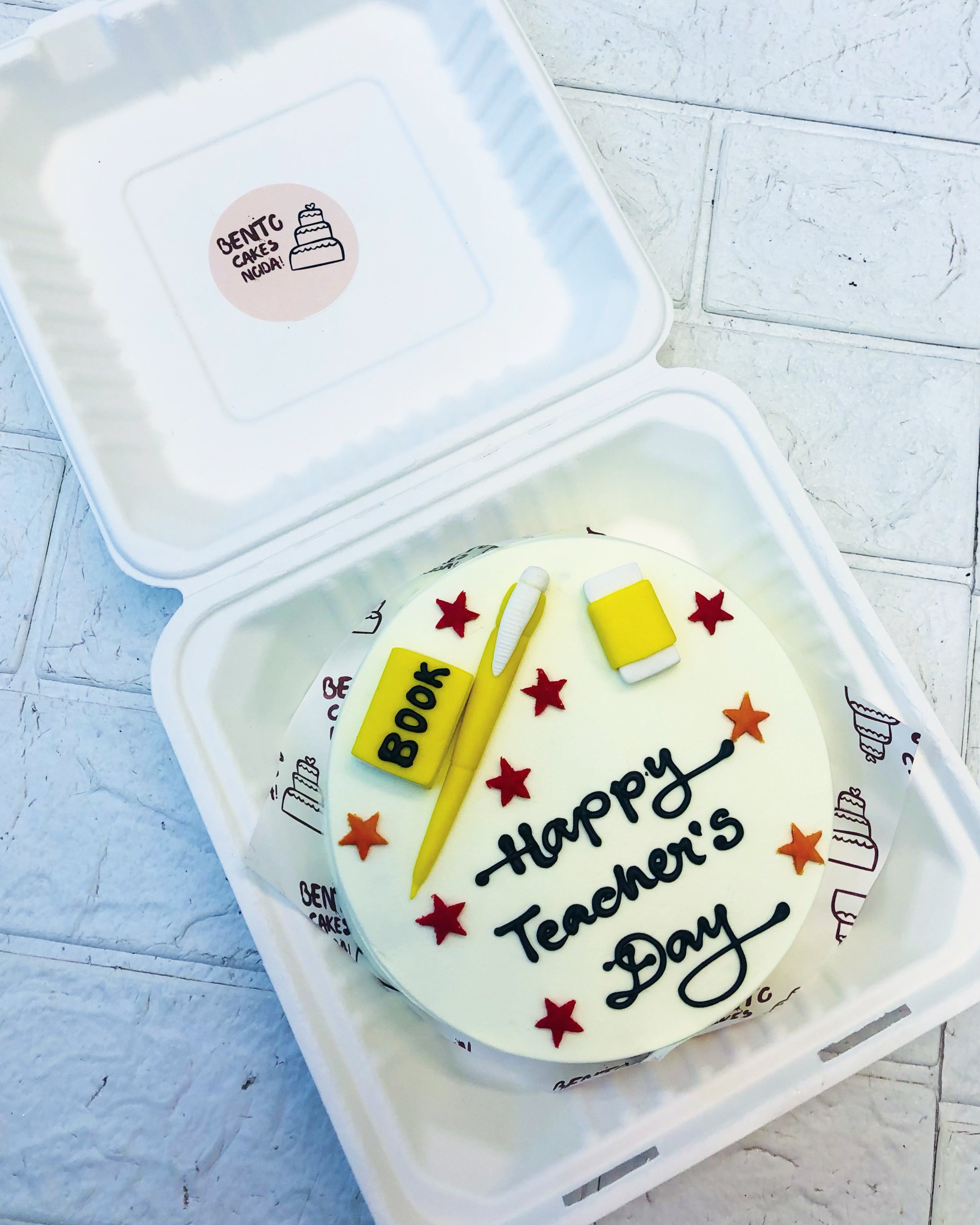 A white bento cake with fonant articles for Teacfher's Day like Book, Pen and Eraser with some pretty stars design.