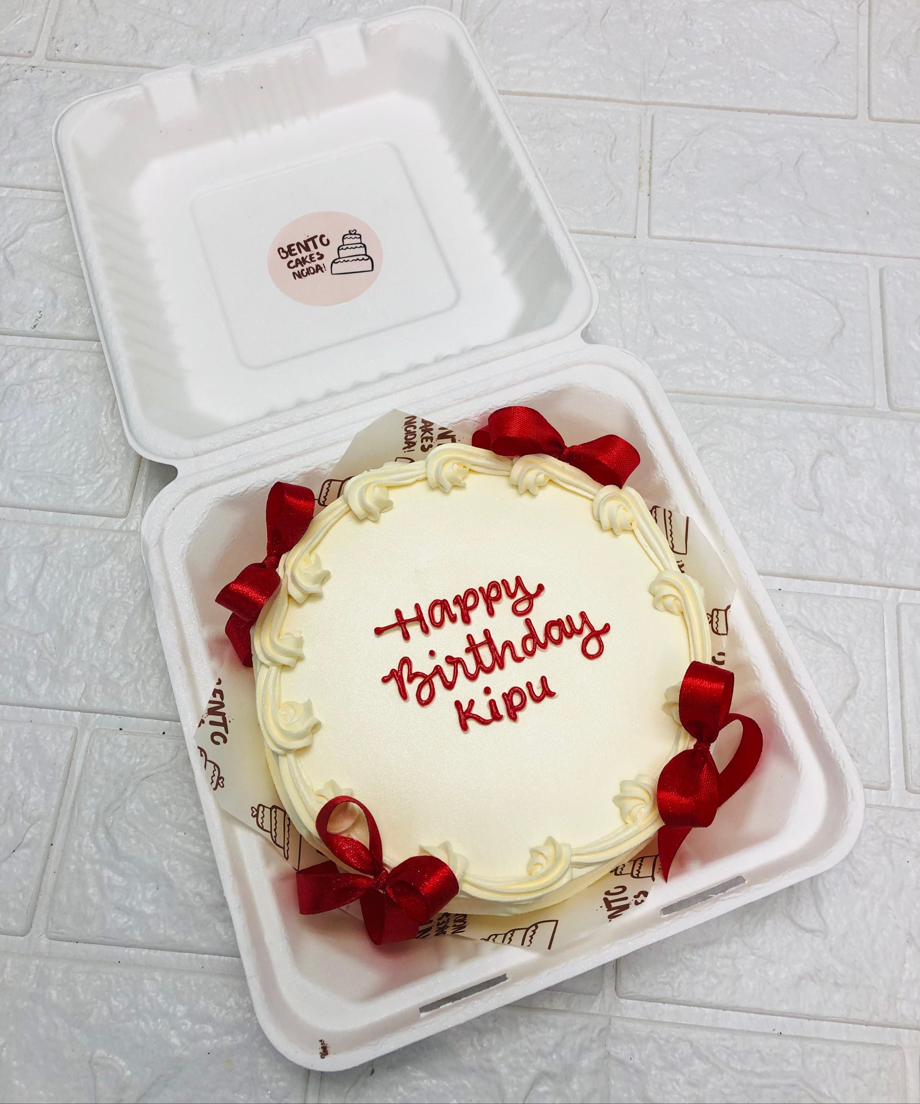 An offwhite birthday bento cake decorated with red bows with red text.
