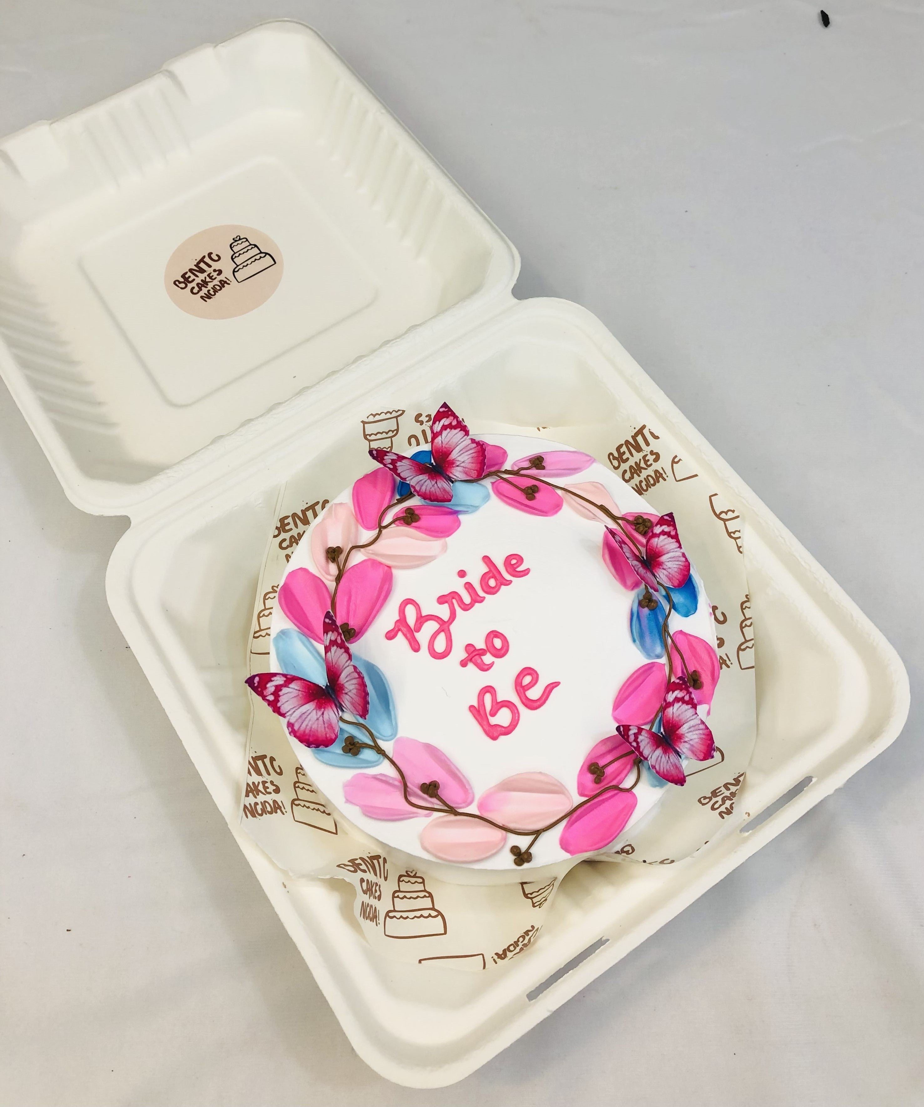 A white bento cake having blue and pink floral design and decorated with pink butterflies.