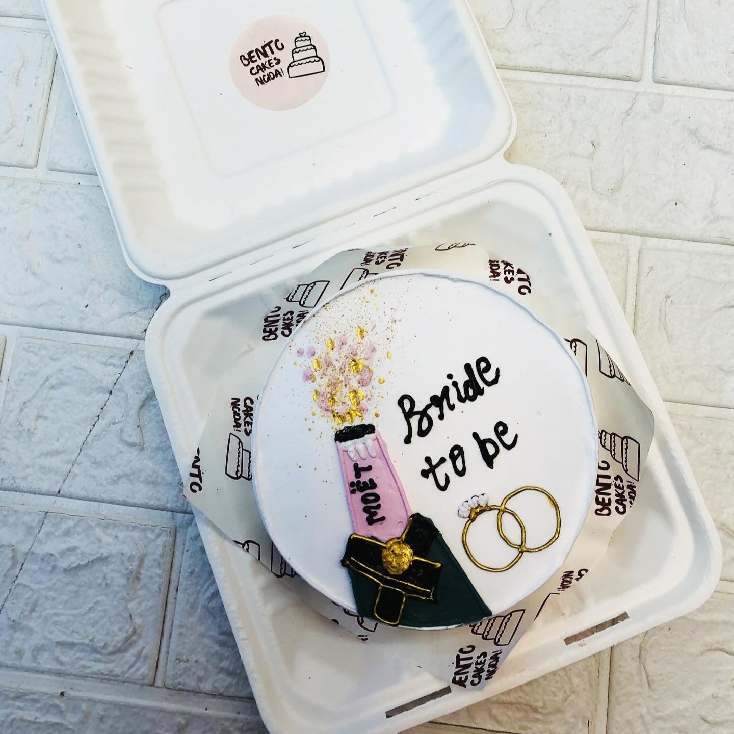 A white bento cake with shampion bottle design and bridal engagement rings design.
