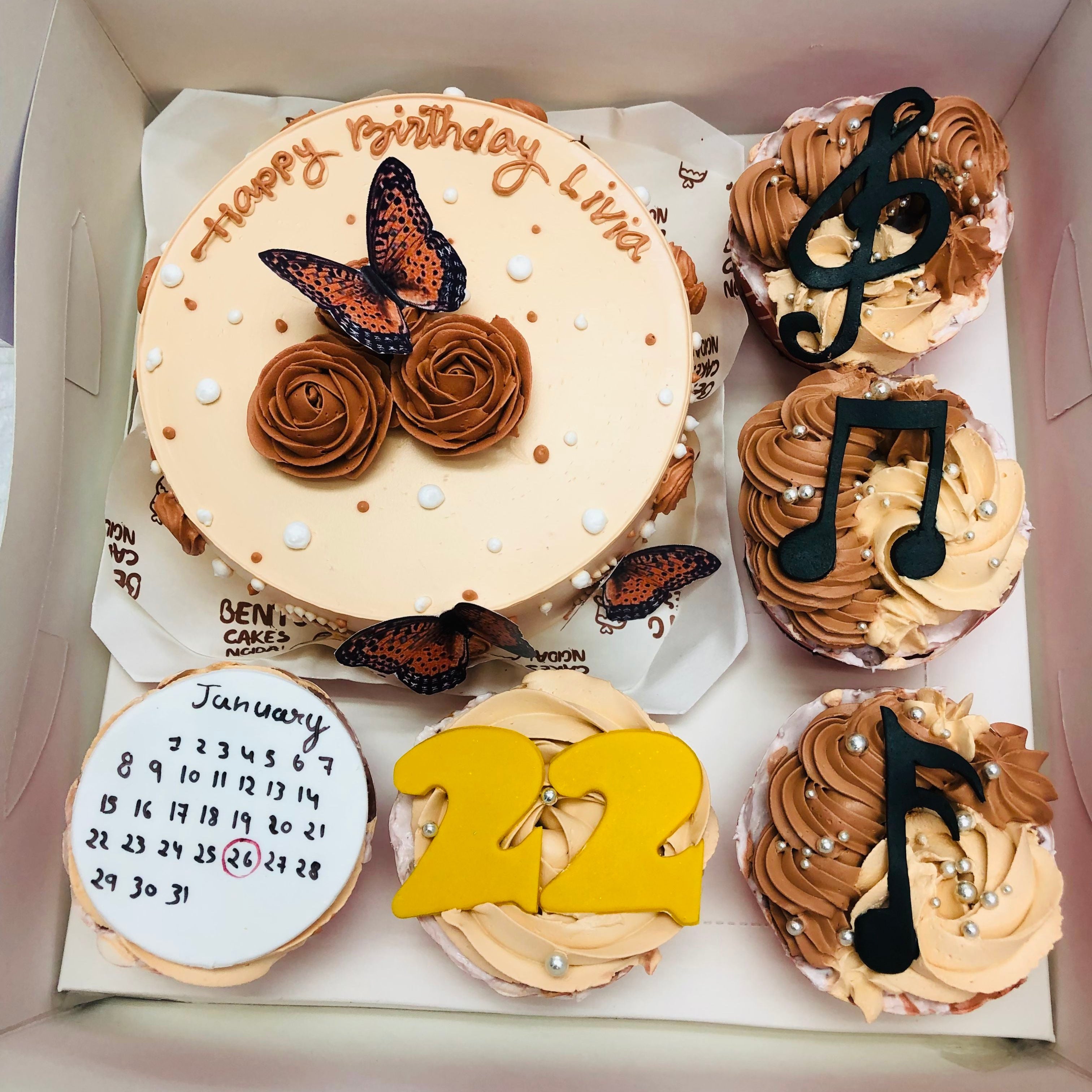 A vibrant assortment of cupcakes in a box next to a charming birthday cake, perfect for a celebration.