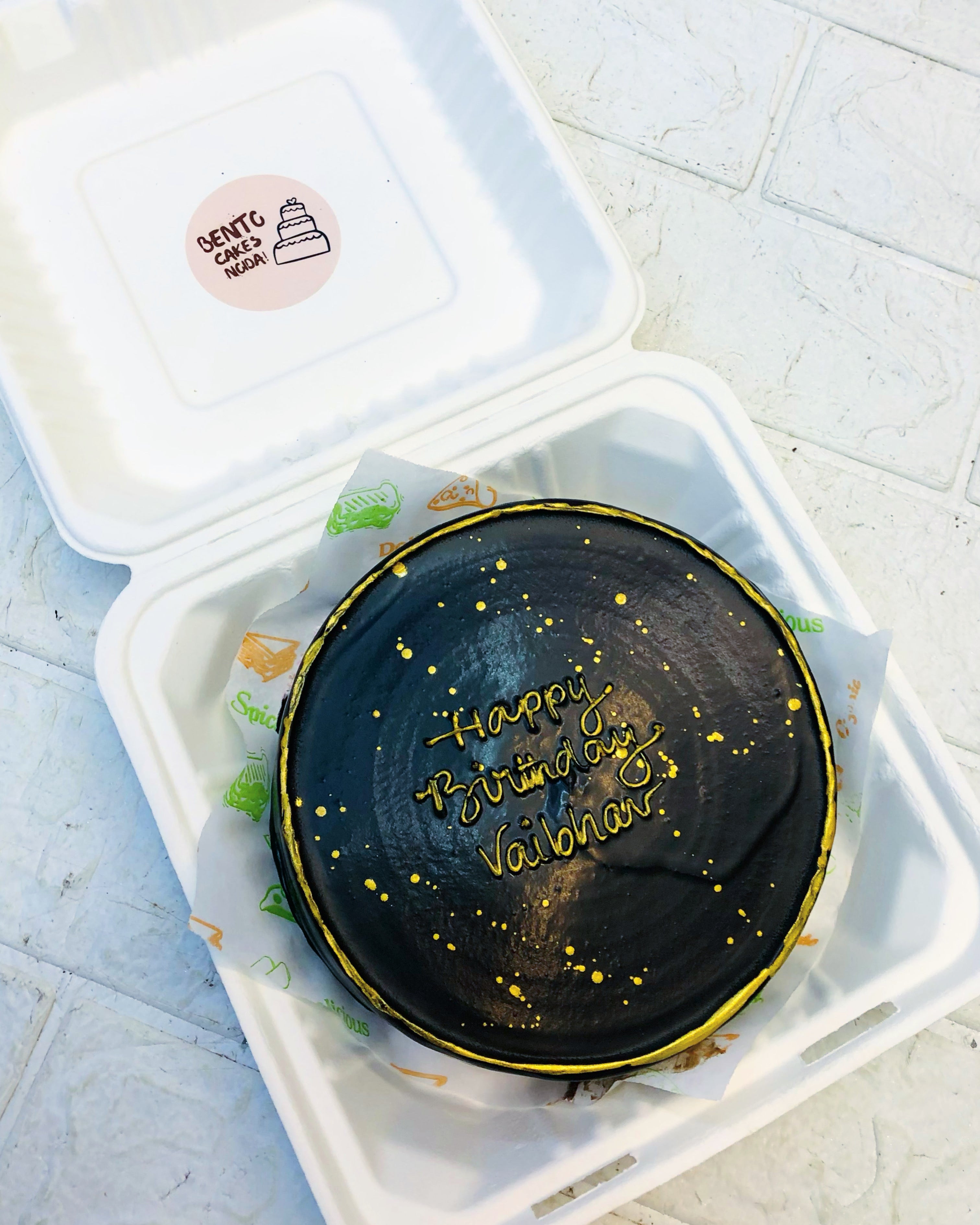 A dark chocolate bento cake with golden birthday text in center with golden boundary.