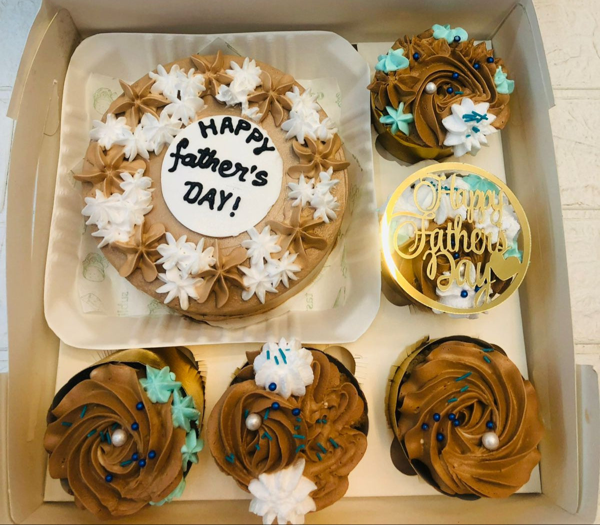 A brown bento vcake with white and brown floral design and 5 cupcakes with brown floral design.