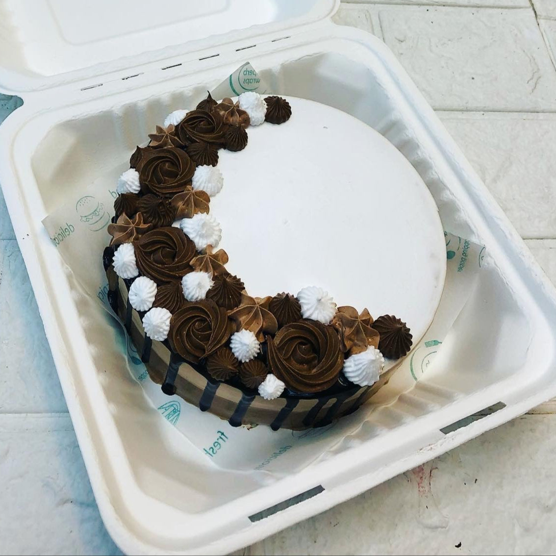 A white cake designed with brown, white truffles on one side of cake.