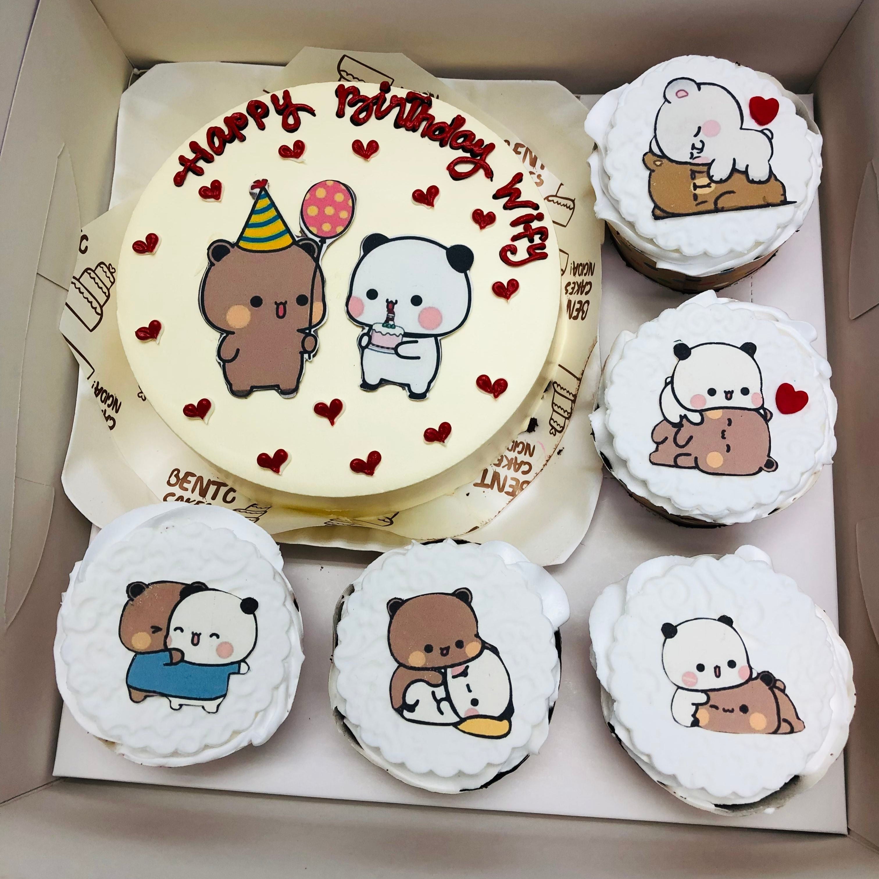 A round white birthday cake with "Happy Birthday Wifey" written in red icing, featuring two adorable bears with balloons and a cake. Accompanied by five cupcakes with bubu dudu themed decorations.