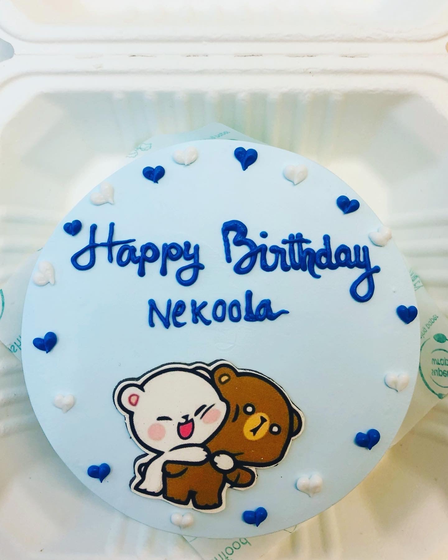 A cool blue cake is decorated with blue and white hearts on it and a Bubu Dudu cartoon character hugging each other placed on it.