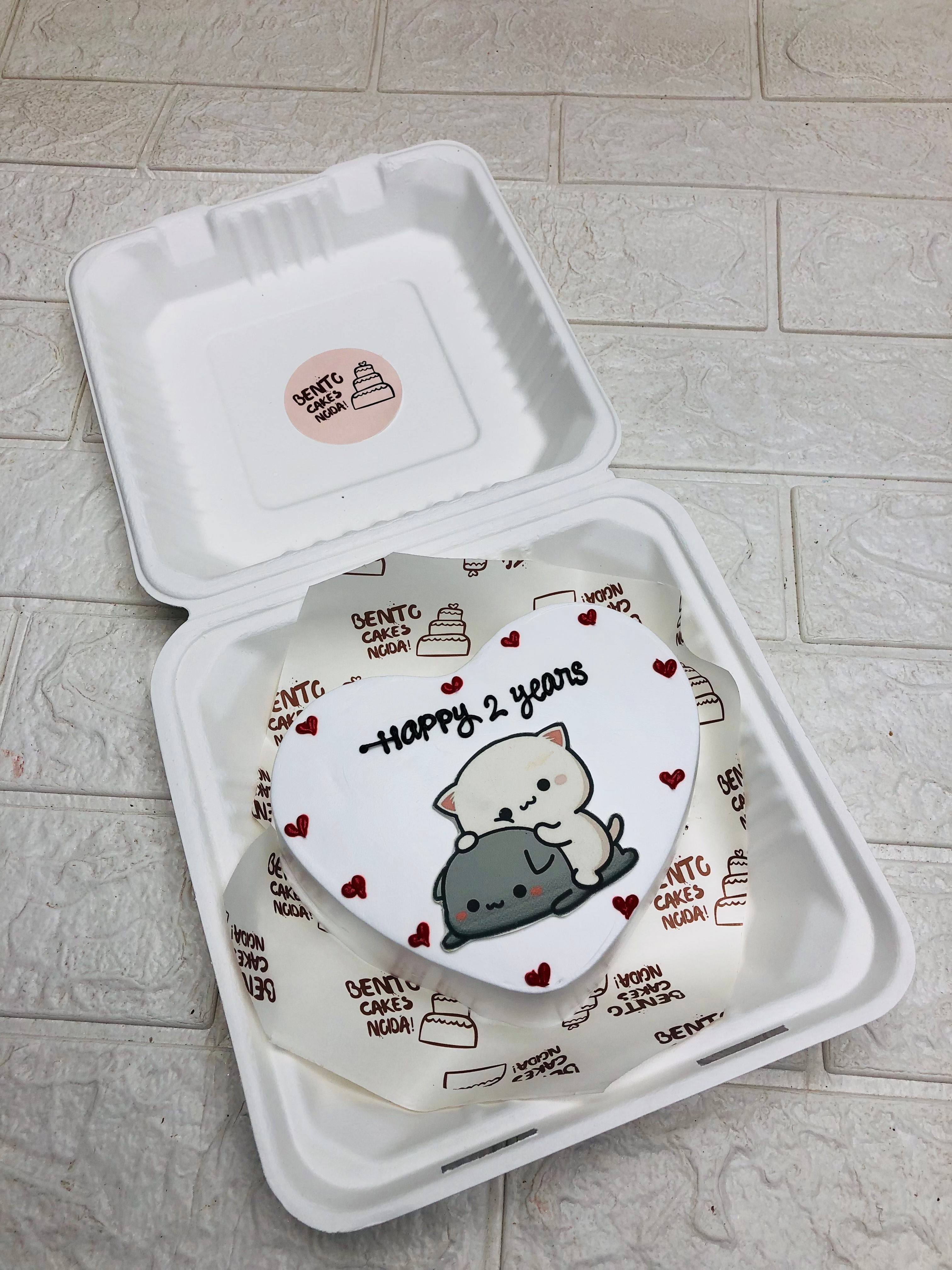 A white heart shaped cakes adorn with cute bubu dudu cartoon sticker and a text "Happy 2 Years" written with black icing and decorated with pretty red hearts.
