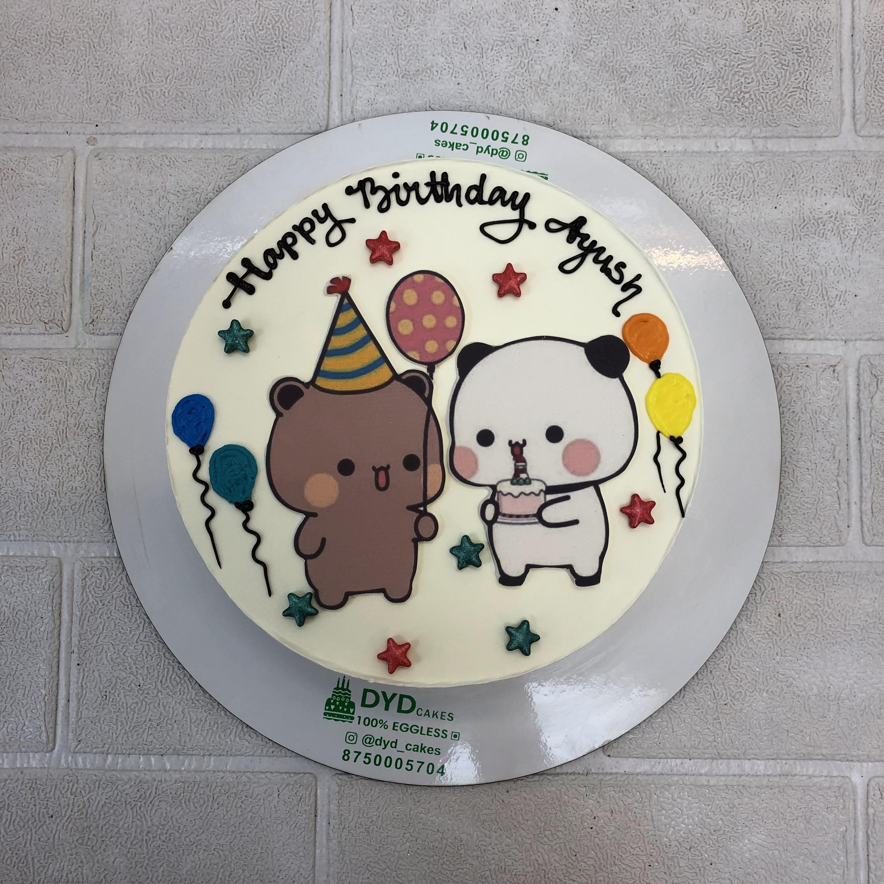 A round white birthday cake decorated with two cartoon bears, one brown with a party hat and balloon, and one white holding a cake. The cake features colorful stars, balloons, and the text "Happy Birthday Ayush."