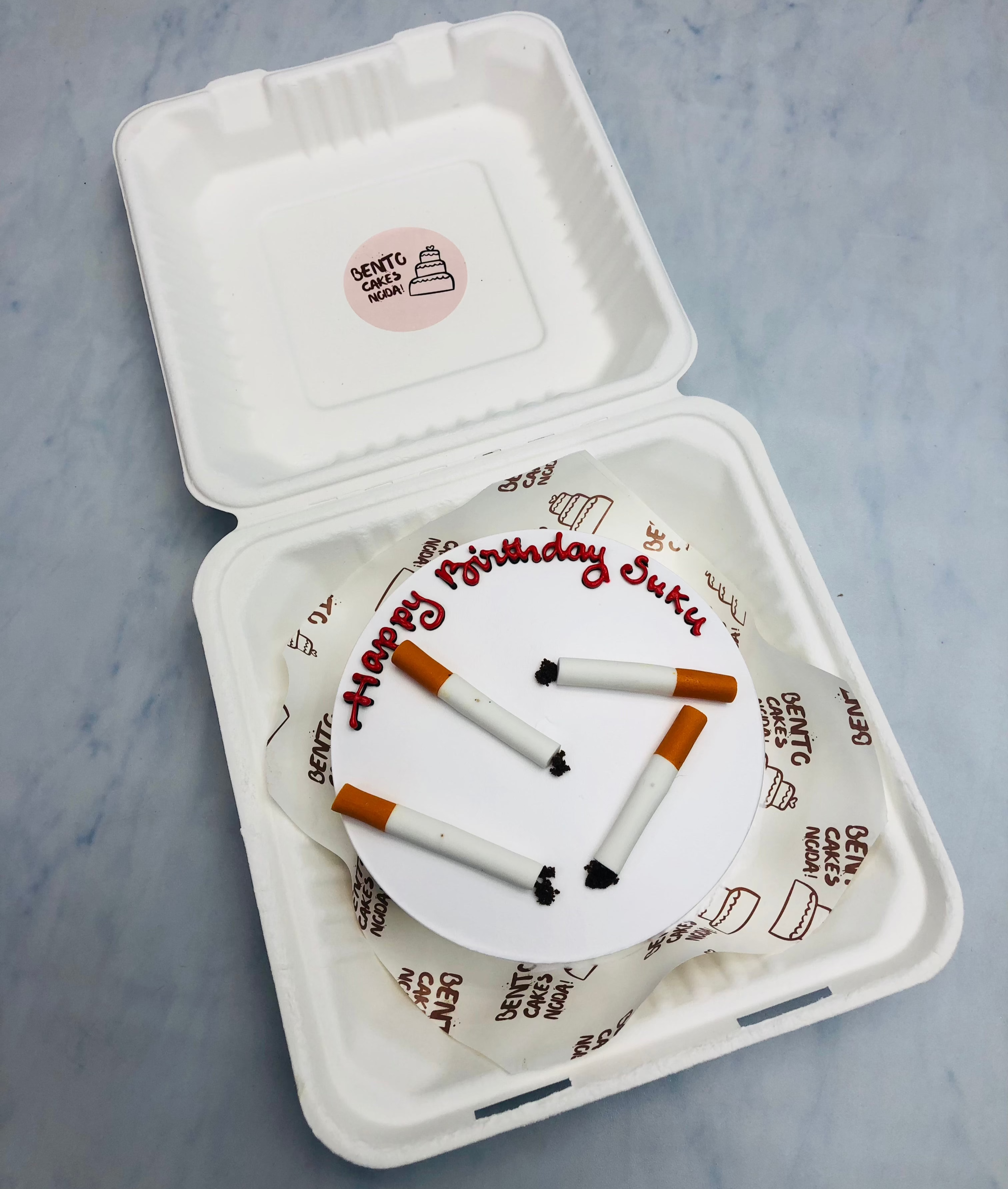  4 burned fondant cigarettes are placed on a white bento cake for birthday.