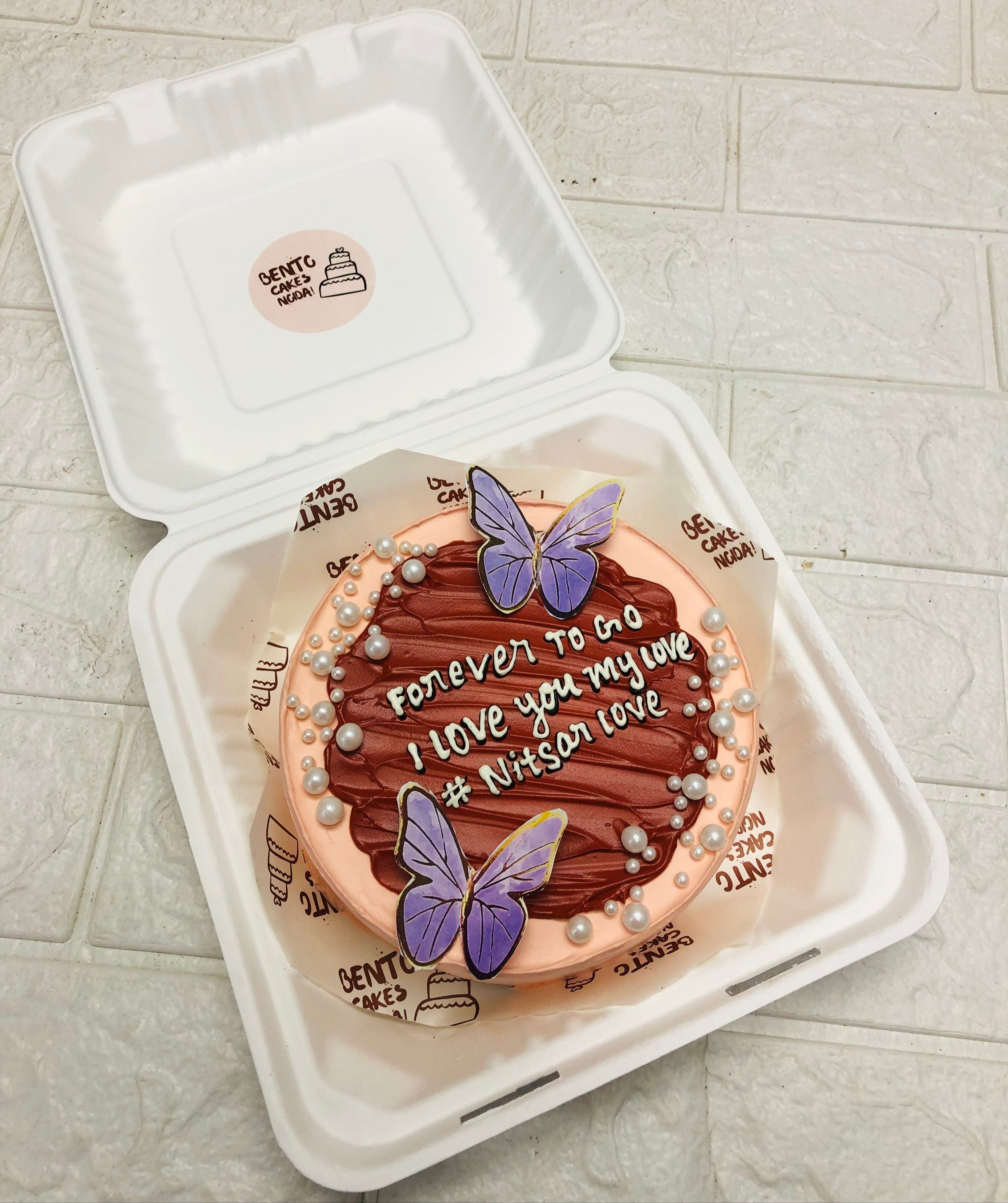 An aesthetic brown shades on a peach color bento cake, decorated with blue butteflies and white sprinkles.